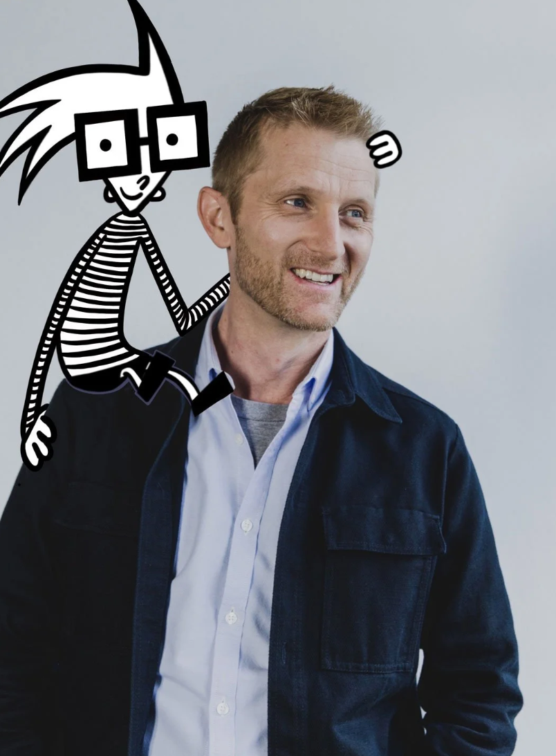 A man with short, light brown hair and a beard, wearing a dark blue jacket and a light-colored shirt, smiling while looking to the side. A cartoon character with spiky hair, glasses, and striped clothing is depicted sitting on his shoulder, smiling and giving a thumbs up.
