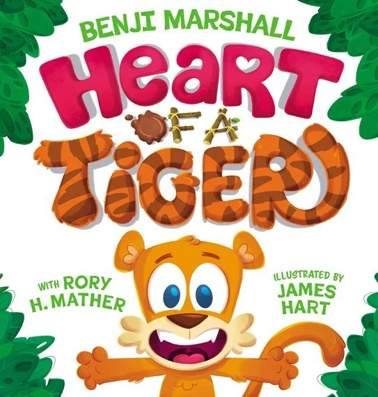 Book cover titled 'Heart Tiger' by Benji Marshall, illustrated by James Hart, featuring a cartoon tiger with big blue eyes and a wide smile, surrounded by green foliage.