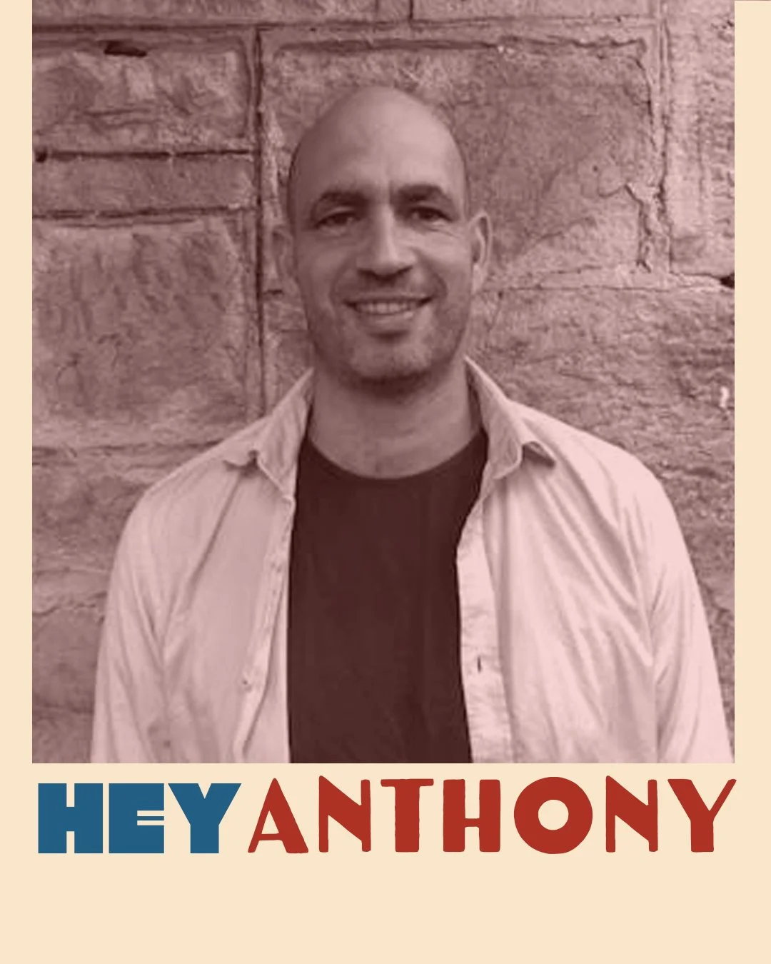 A man with a shaved head and a short beard, smiling, standing in front of a stone wall, wearing a light-colored open shirt over a dark t-shirt, with the text "Hey Anthony" in bold blue and red letters below the photo.