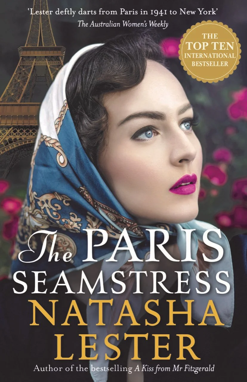 Book cover of 'The Paris Seamstress' by Natasha Lester. It features a close-up of a woman's face with blue eyes, dark brown hair, bright pink lipstick, wearing a silk headscarf with a blue and gold pattern. In the background, there is an image of the Eiffel Tower with pink flowers. A gold badge indicates it as a top ten international bestseller.