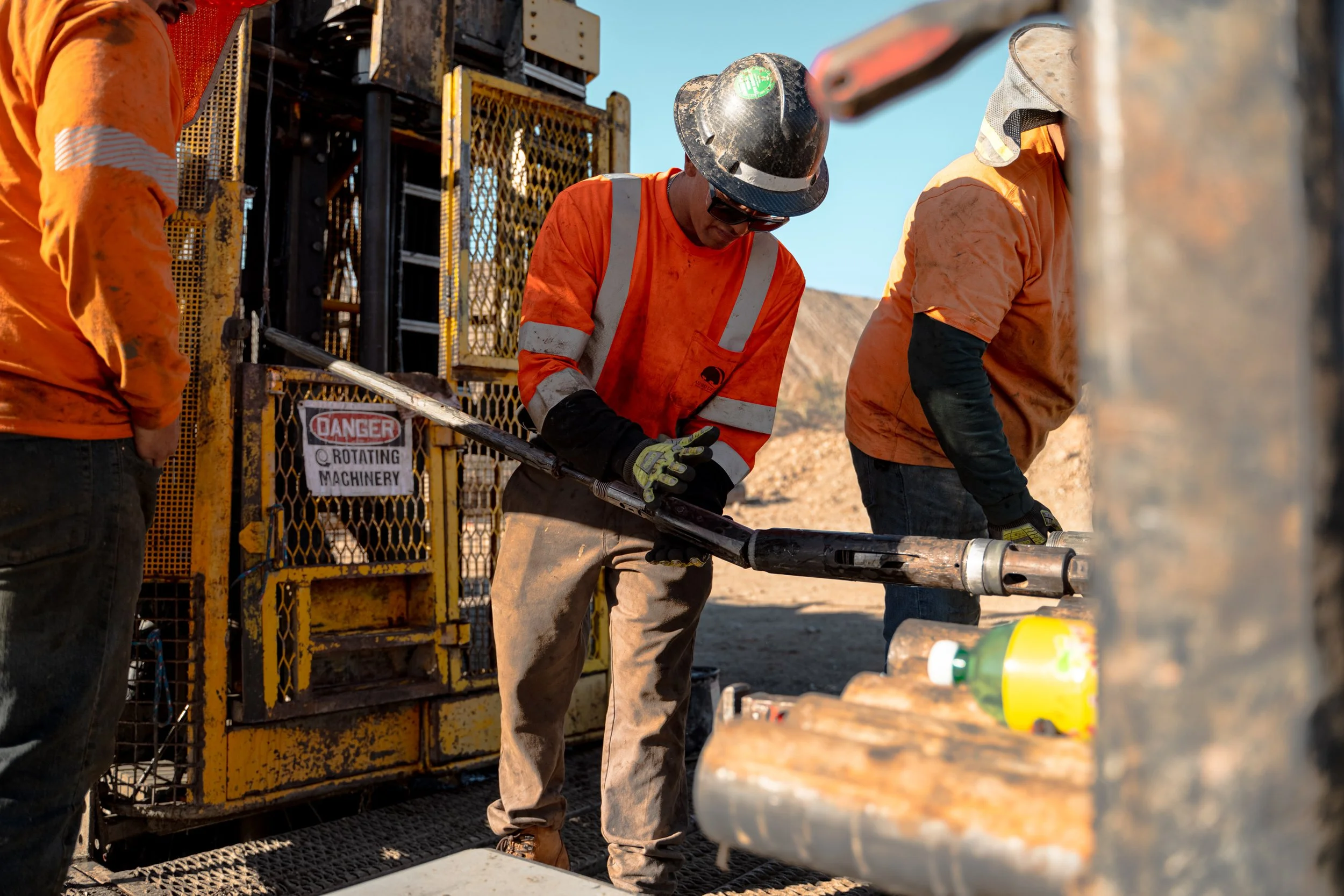 Workers in orange safety vests and helmets operating drilling equipment on a construction site.