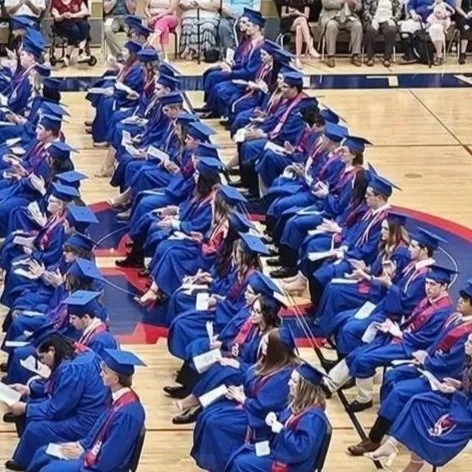 Graduates in blue caps and gowns seated in rows during a ceremony
