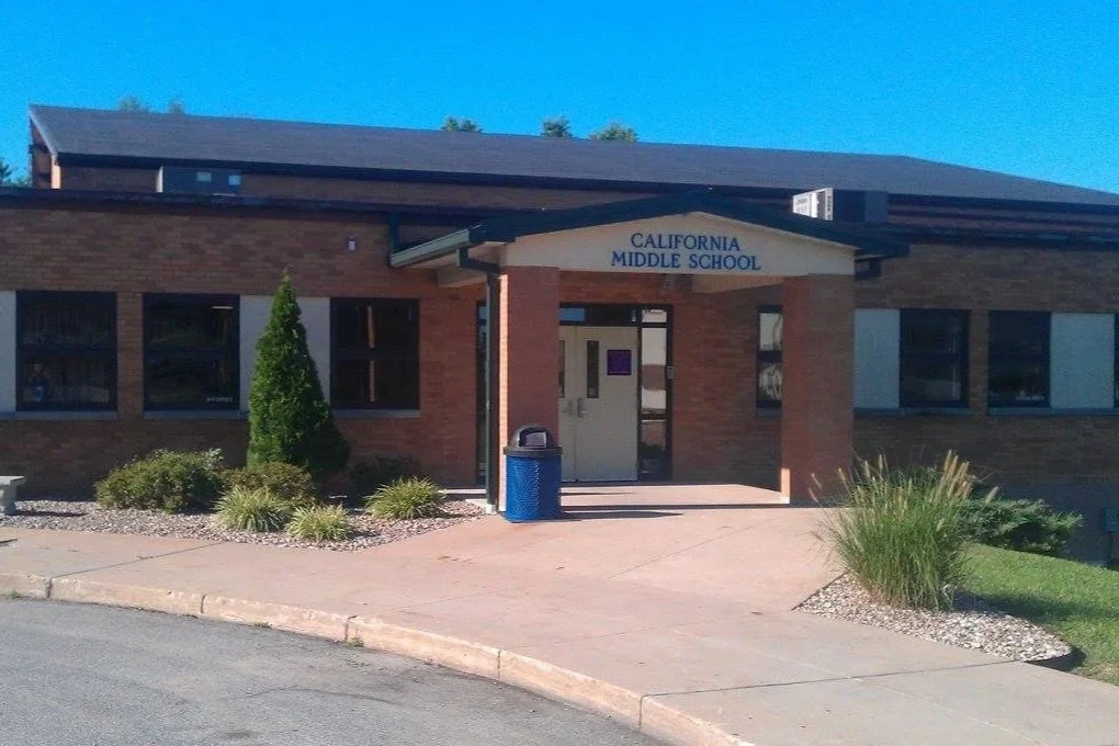 Front view of California Middle School building with brick exterior, a covered entrance, and landscaping including bushes and grass.