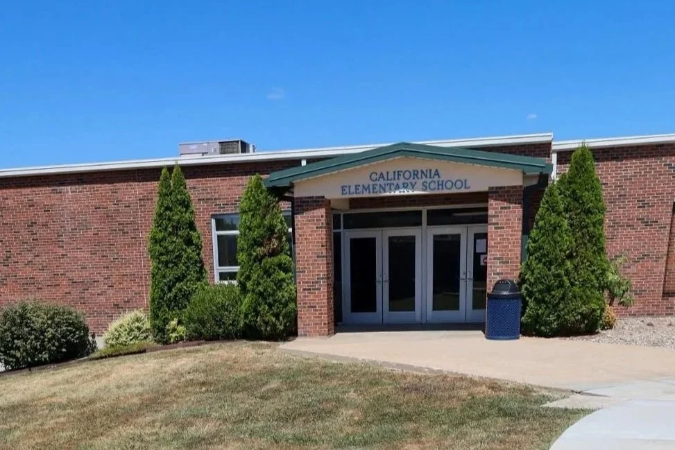 Exterior of California Elementary School building with brick walls, green trees, and a blue sky.