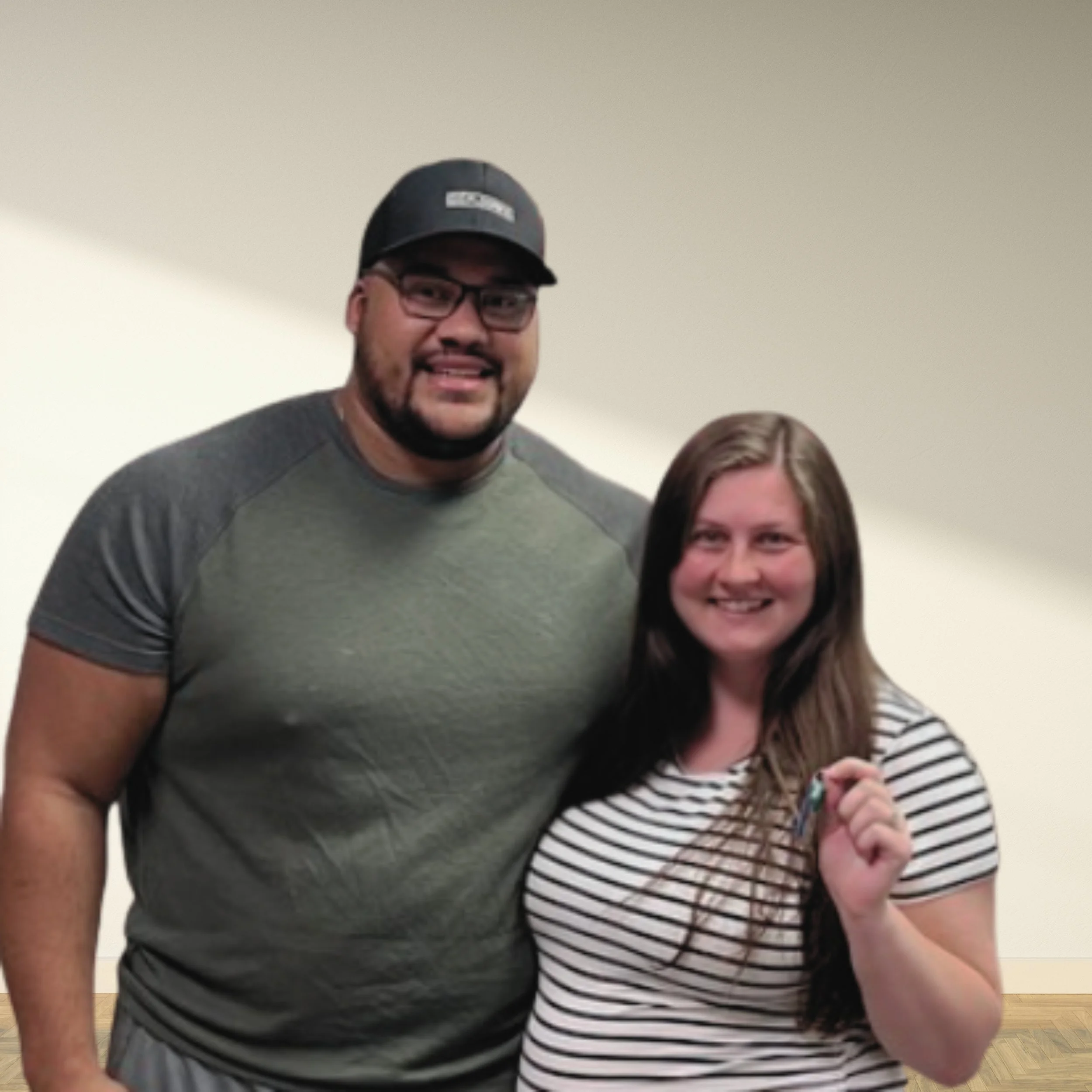A man wearing glasses and a black cap standing next to a woman with long brown hair holding a set of keys, both smiling.