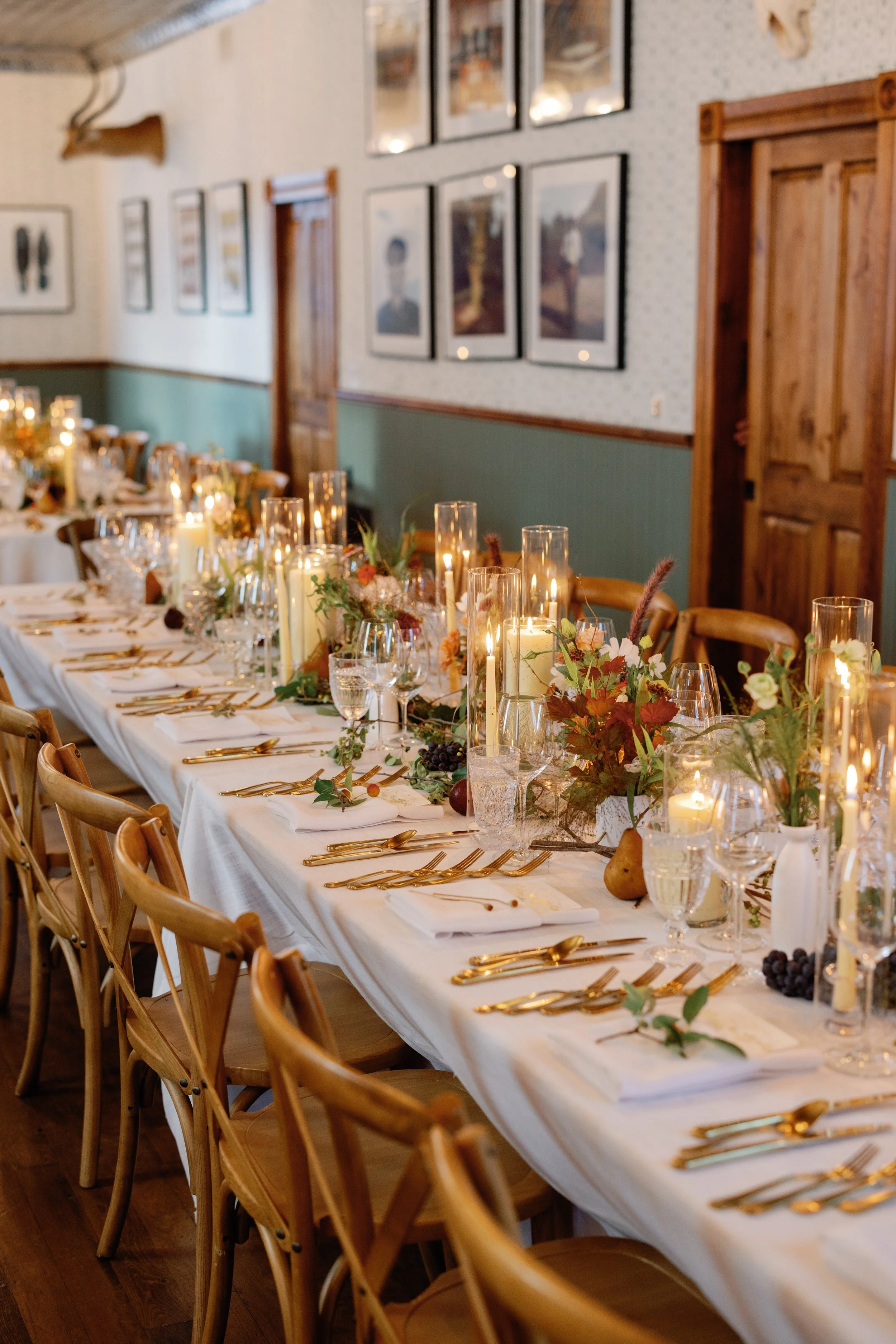 A long banquet table decorated with candles, floral arrangements, and elegant tableware in a rustic dining room.