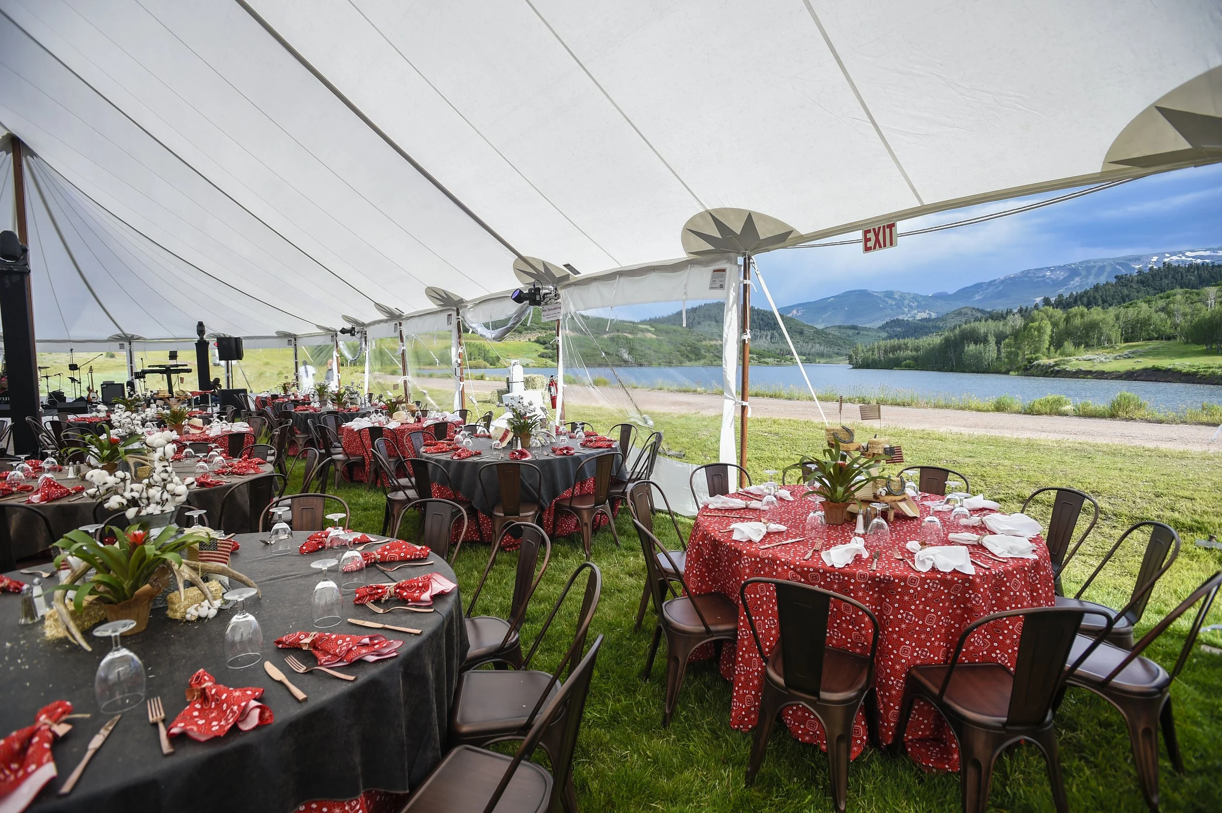 Outdoor event setup with tables decorated for a celebration next to a lake and mountain view.