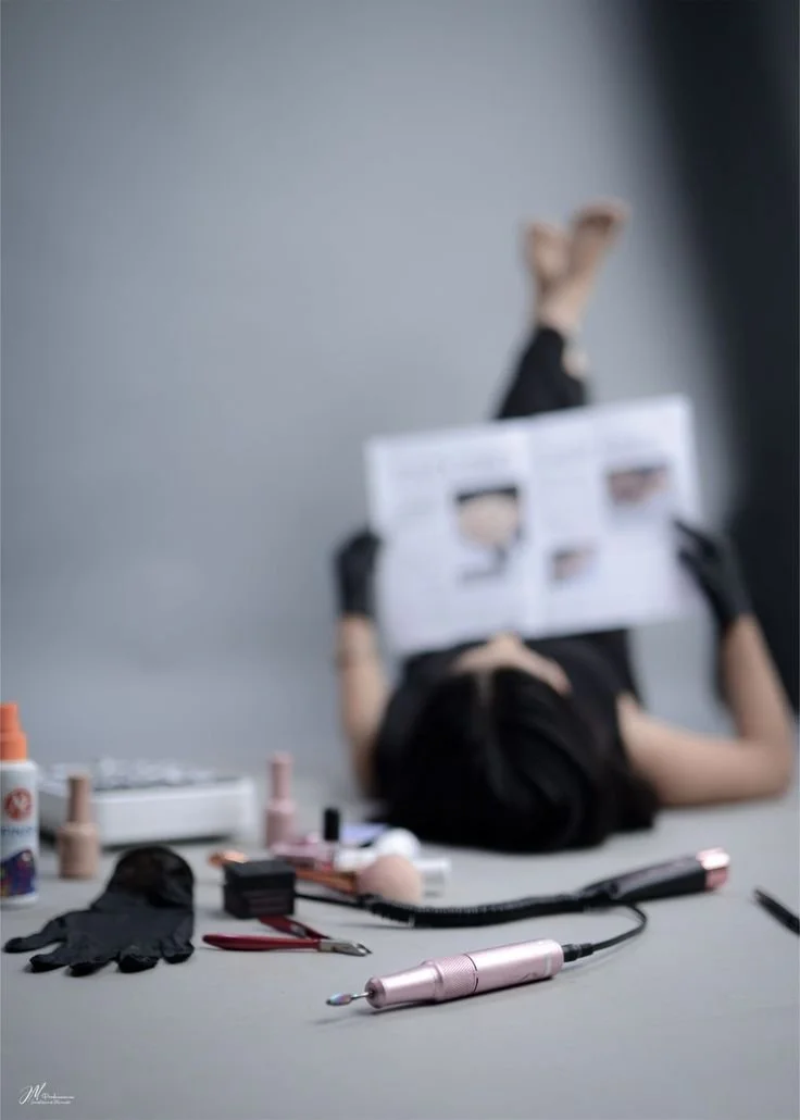 Una donna strisciante su un pavimento con vari strumenti e prodotti per unghie, che tiene un foglio con immagini di design per unghie.