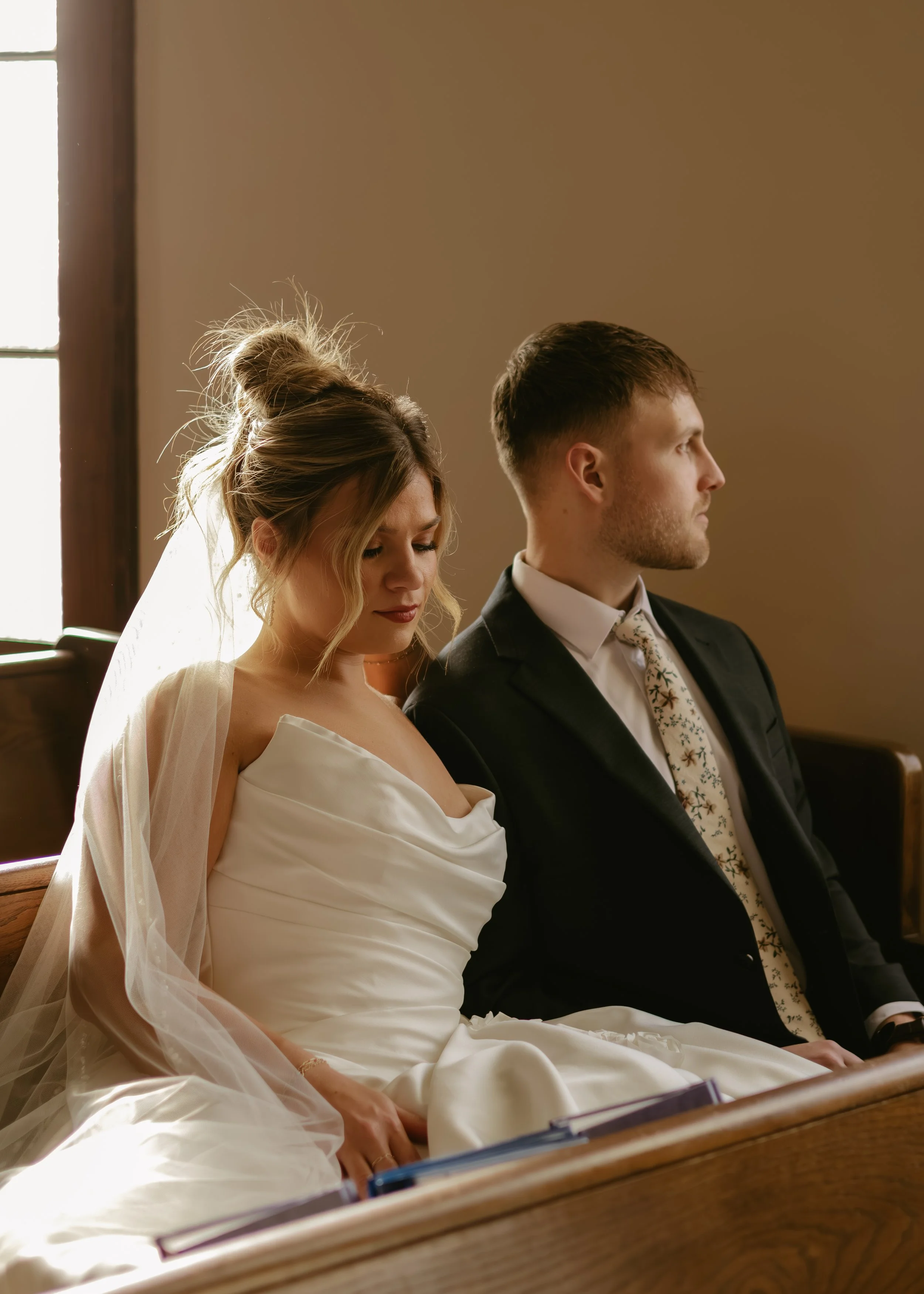 Bride and groom sitting in church, with heads bowed and eyes closed, during a wedding ceremony.