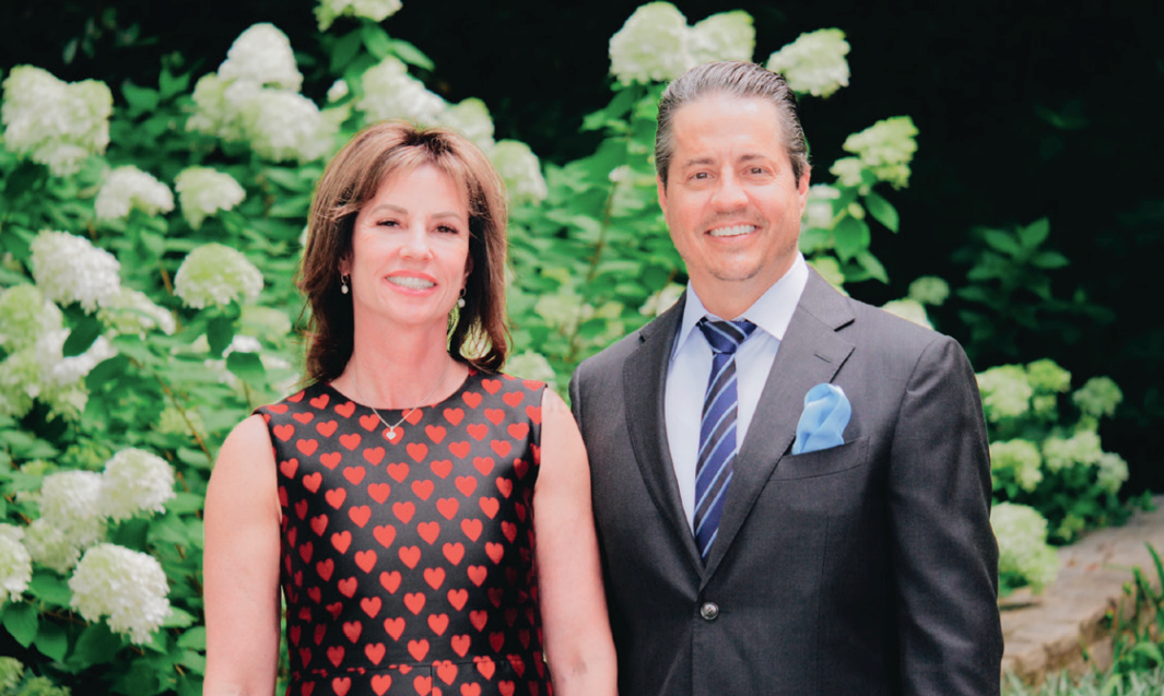 A woman and a man standing outdoors near white hydrangea flowers, smiling at the camera. Tammy and Sean Frith of Cross Country Mortgage | Florida Division