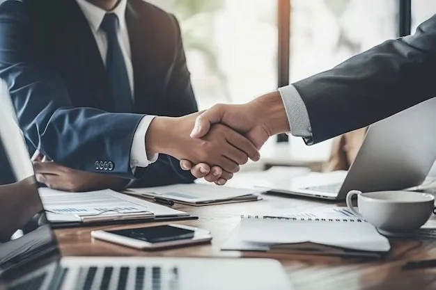 Two people in suits shaking hands across a desk in a business meeting.