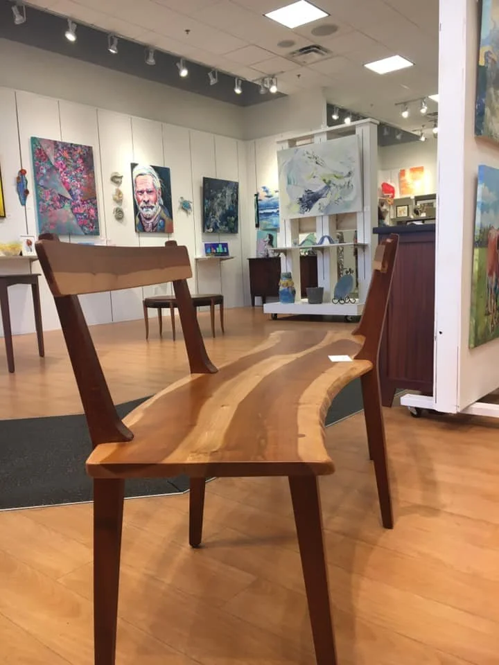 Wooden bench with a natural live edge design in an art gallery with paintings on the wall.