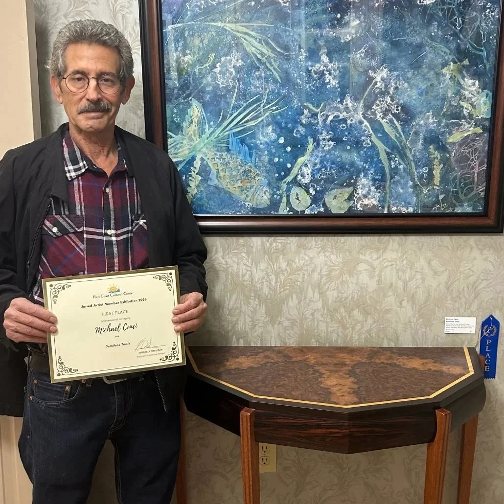 An older man with gray hair, glasses, and a mustache holding a first-place certificate, standing next to a custom Michael Cenci console table.