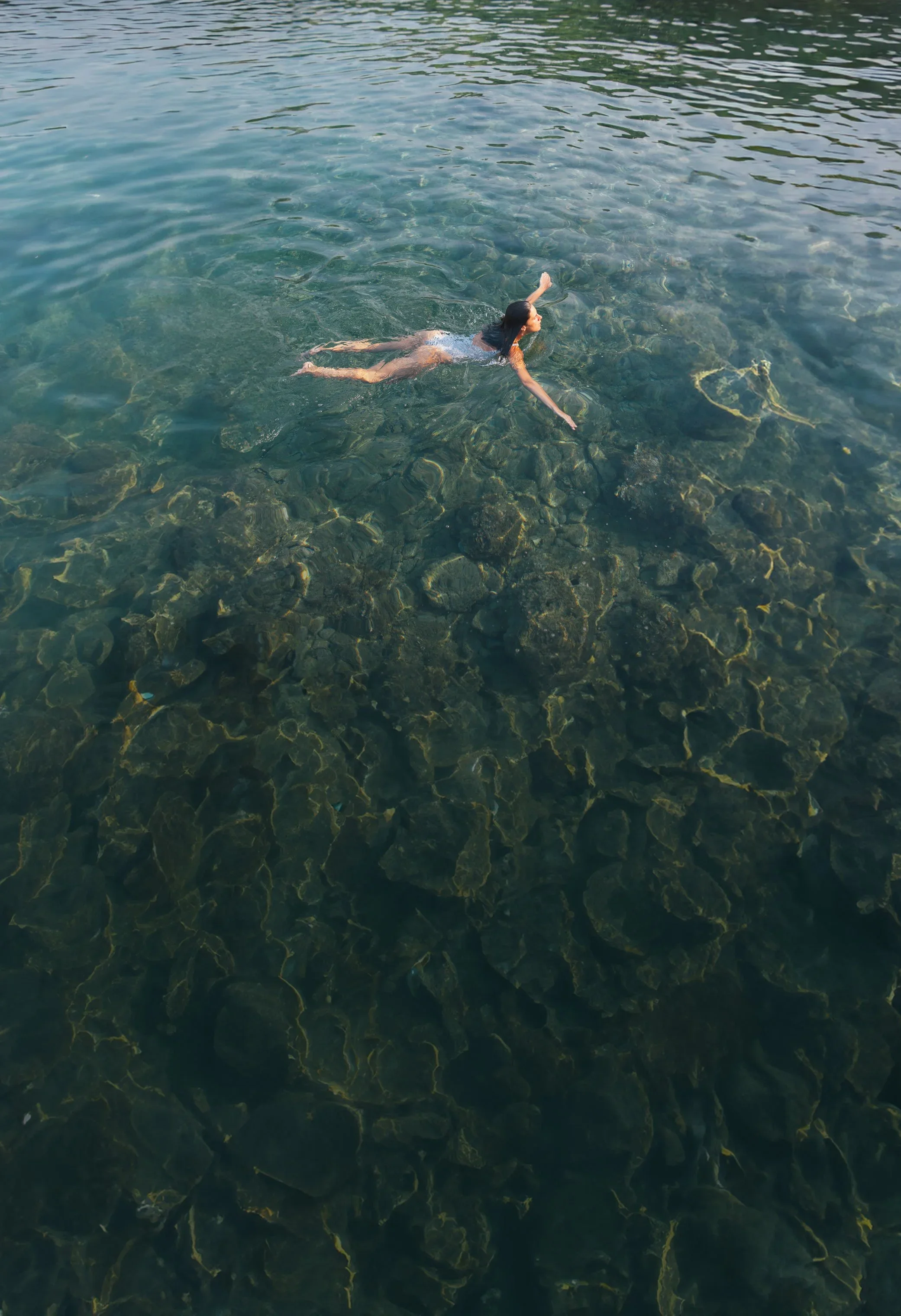 Woman swimming in clear water over rocky riverbed.
