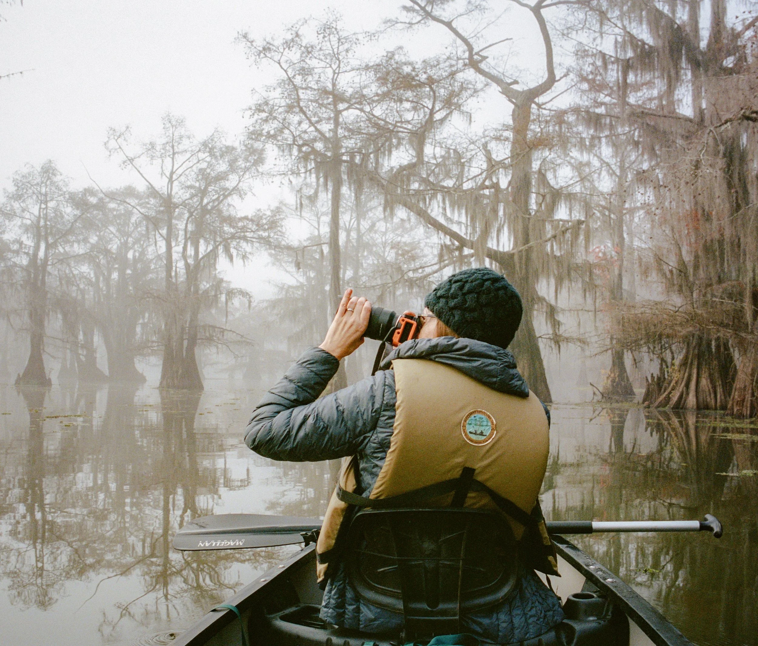 Photographer Robin May-Davis sitting in a canoe along the Texas shoreline, preparing to take a photo, carefully framing a Great Egret with her telephoto lens.