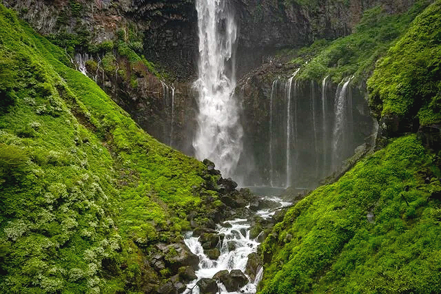 Kegon Falls, a 320-foot-tall waterfall cascading over a cannon of lush, greenery interlaced with rocks, during spring migratory season. Located in Nikkō National Park near the city of Nikkō, Japan.