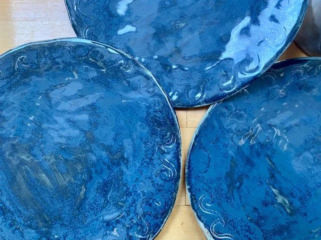 Three blue glass plates with decorative rims, one stacked partially on top of the other on a wooden surface.