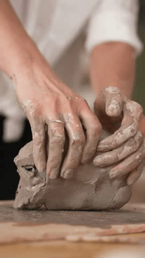Hands kneading clay on a wooden surface.