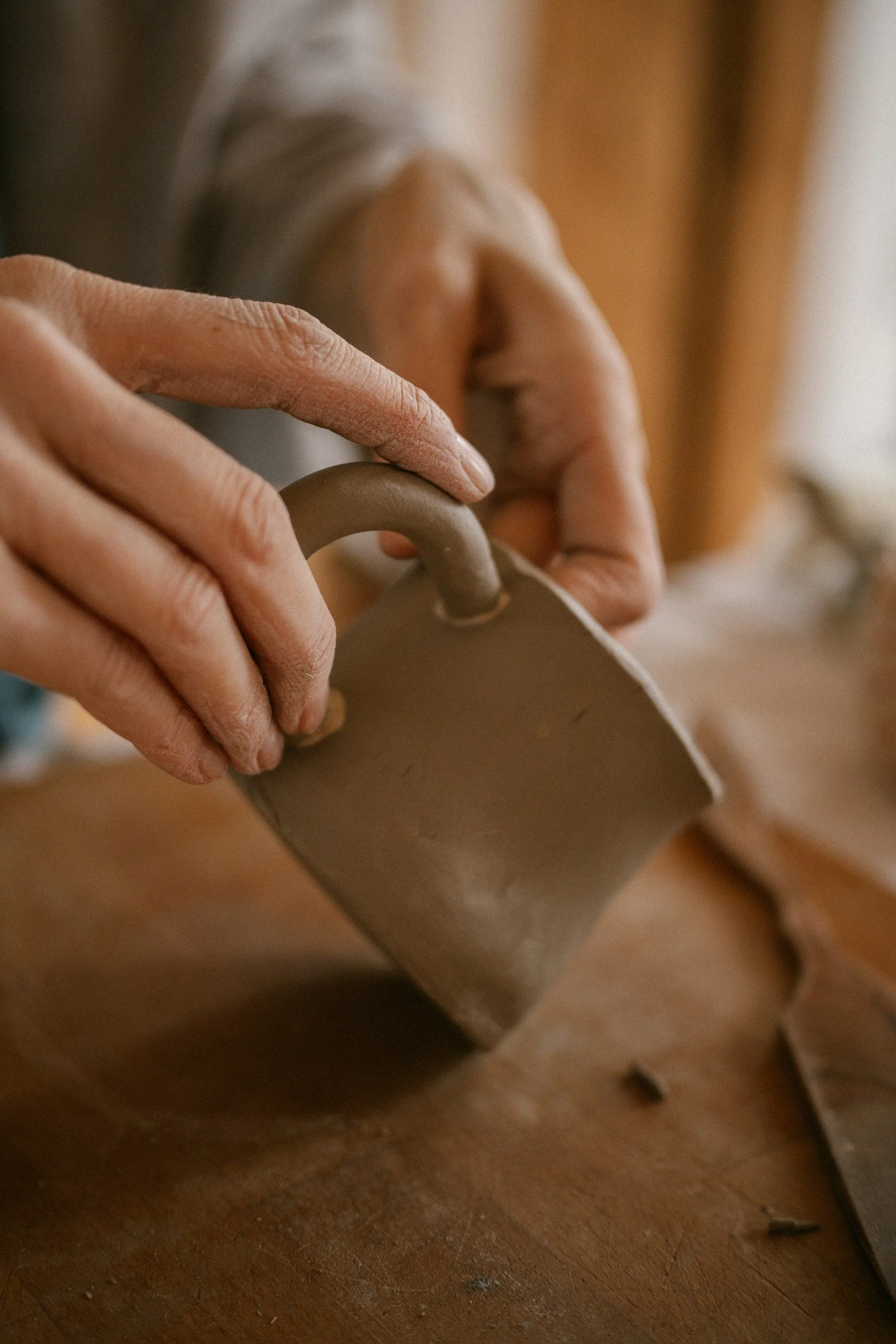 Close-up of a person shaping a clay mug on a pottery wheel by hand, with a wooden surface underneath.