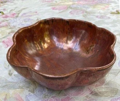 A brown ceramic bowl with a scalloped edge, sitting on a floral tablecloth.