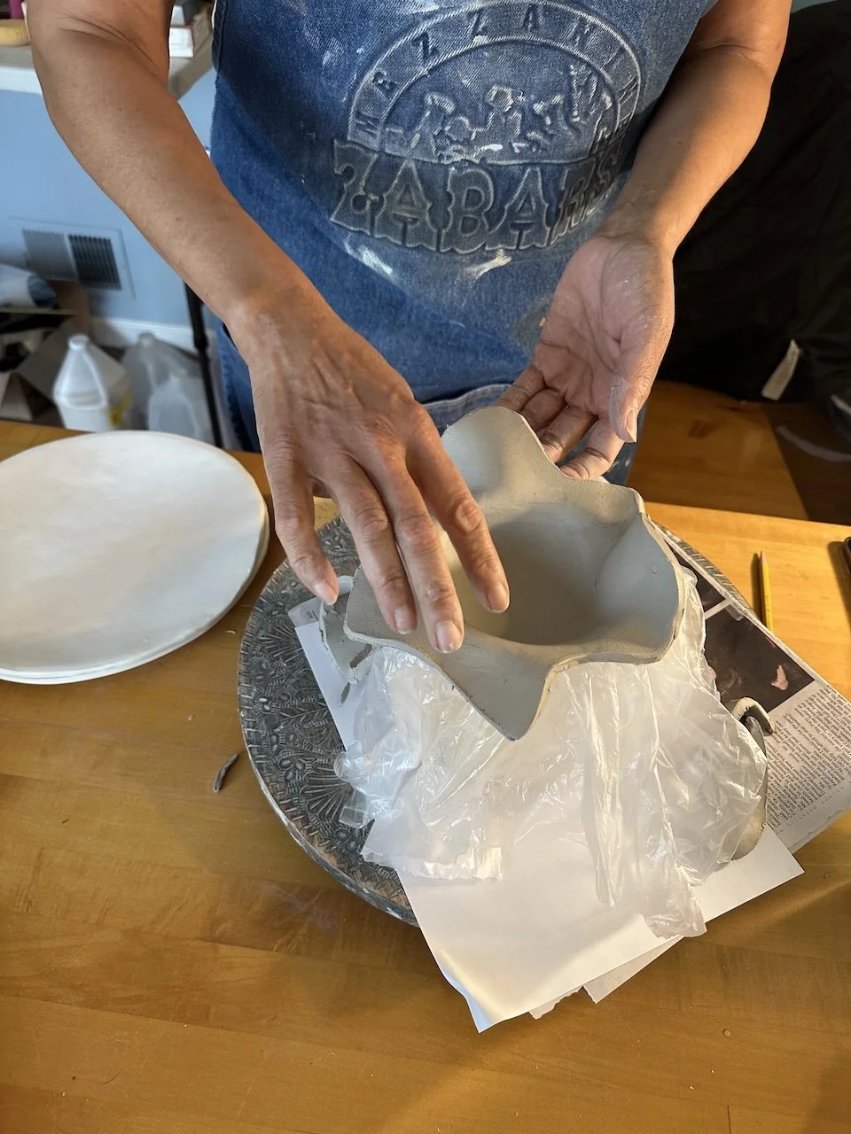 Person shaping clay into a star-shaped mold in a pottery wheel studio, with finished plates nearby.
