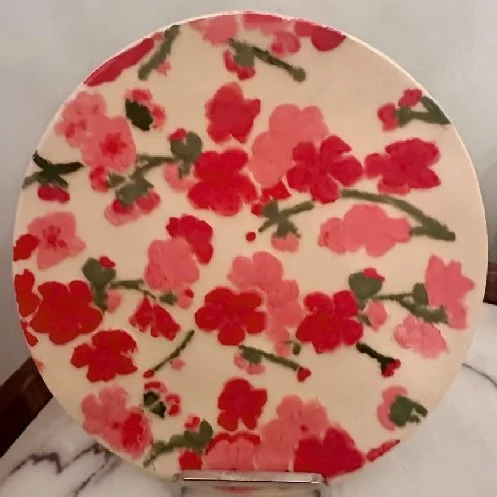 A round ceramic plate with a floral pattern of pink and red flowers with green leaves.