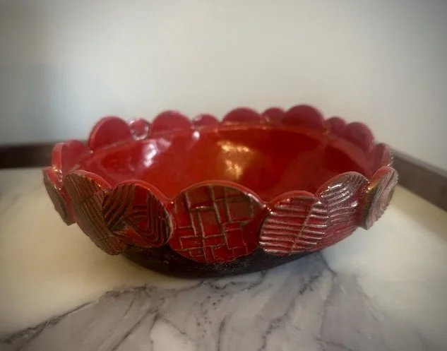 A decorative bowl with a red, scalloped edge and heart-shaped designs on the exterior, placed on a marble surface.
