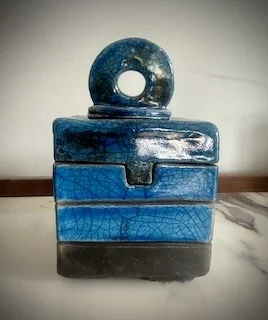 A blue, textured, ring-shaped object placed on top of a three-tiered blue and black wooden box.