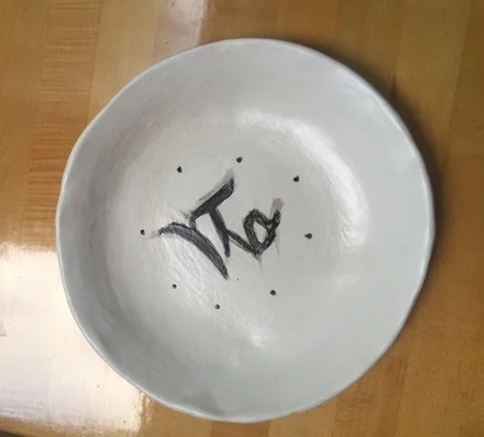 A round ceramic bowl with the word 'Tea' painted inside and small black dots surrounding the word, placed on a wooden surface.