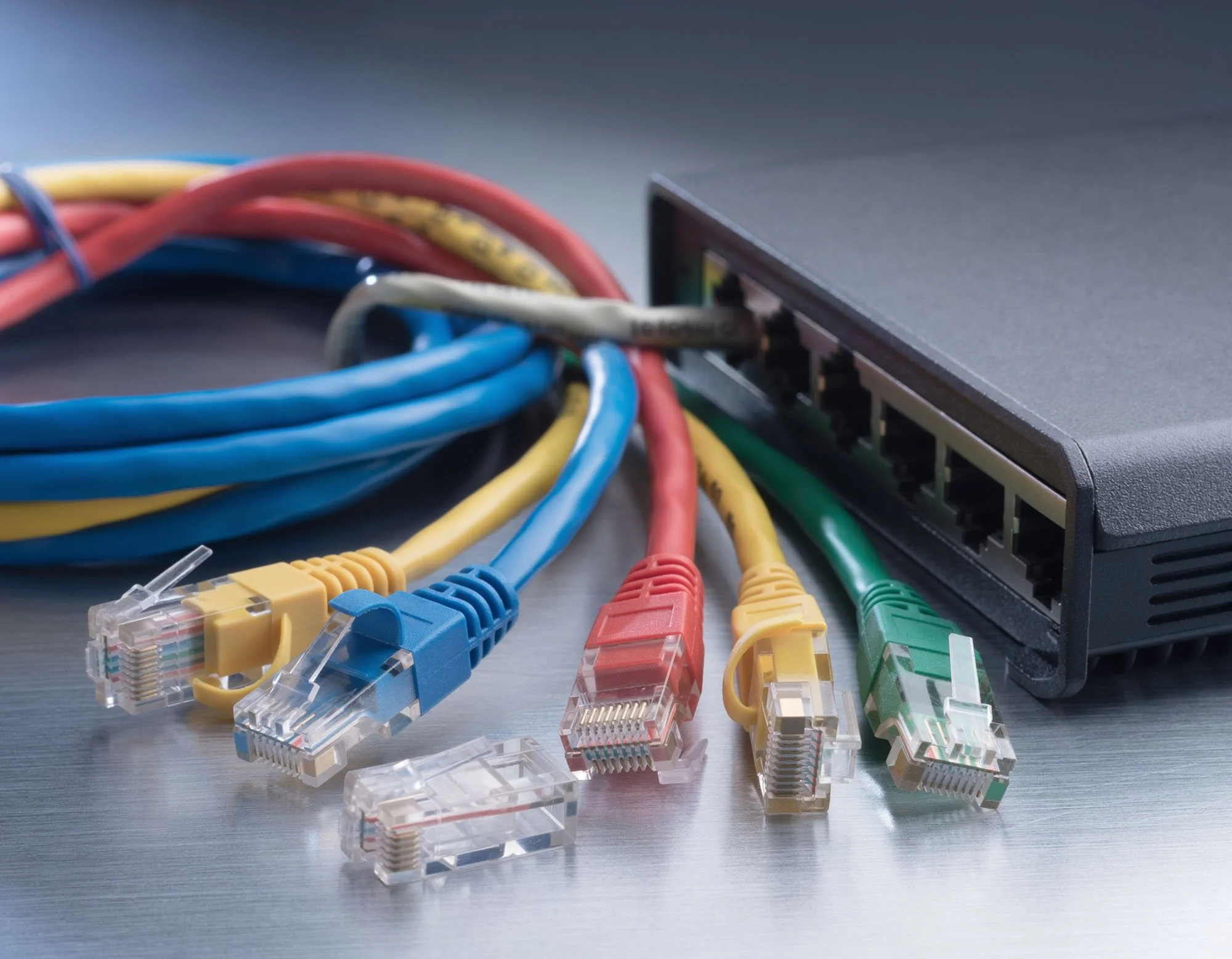 Multicolored Ethernet cables connected to a network switch on a gray surface.