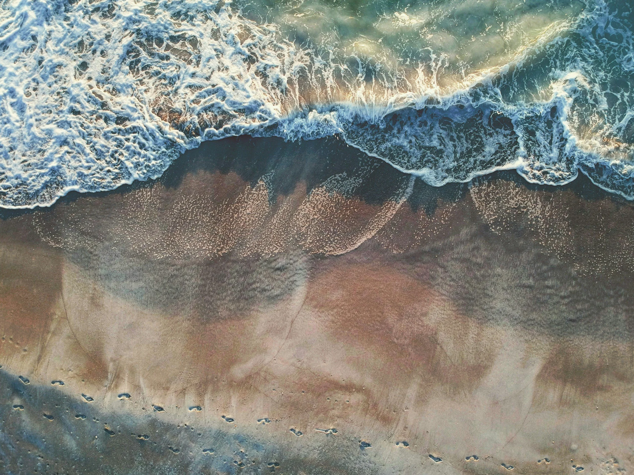 Aerial view of ocean waves crashing onto a sandy beach with a faint overlay of a woman's face.