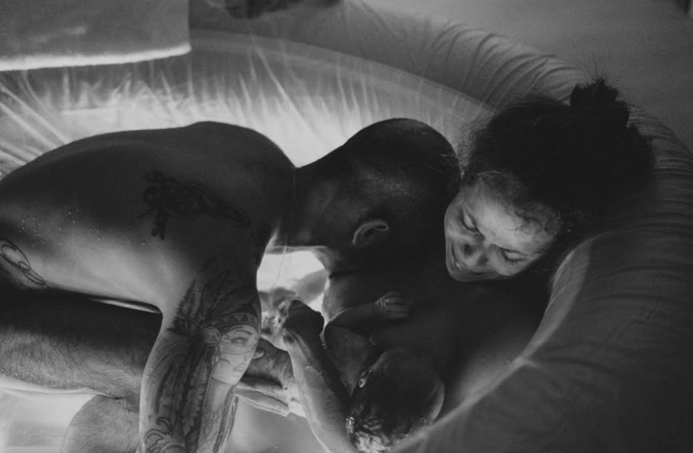 Tattooed man and woman smiling, sharing a close moment on a bed, black and white photo
