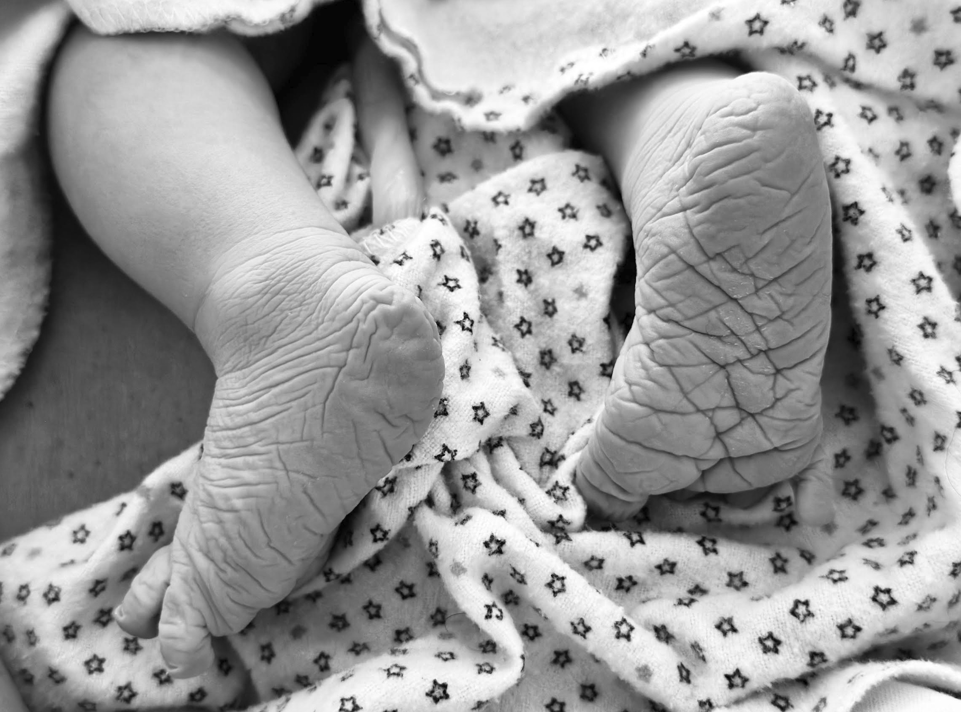 Close-up black and white photo of a baby's tiny hand gripping a small blanket with star pattern.