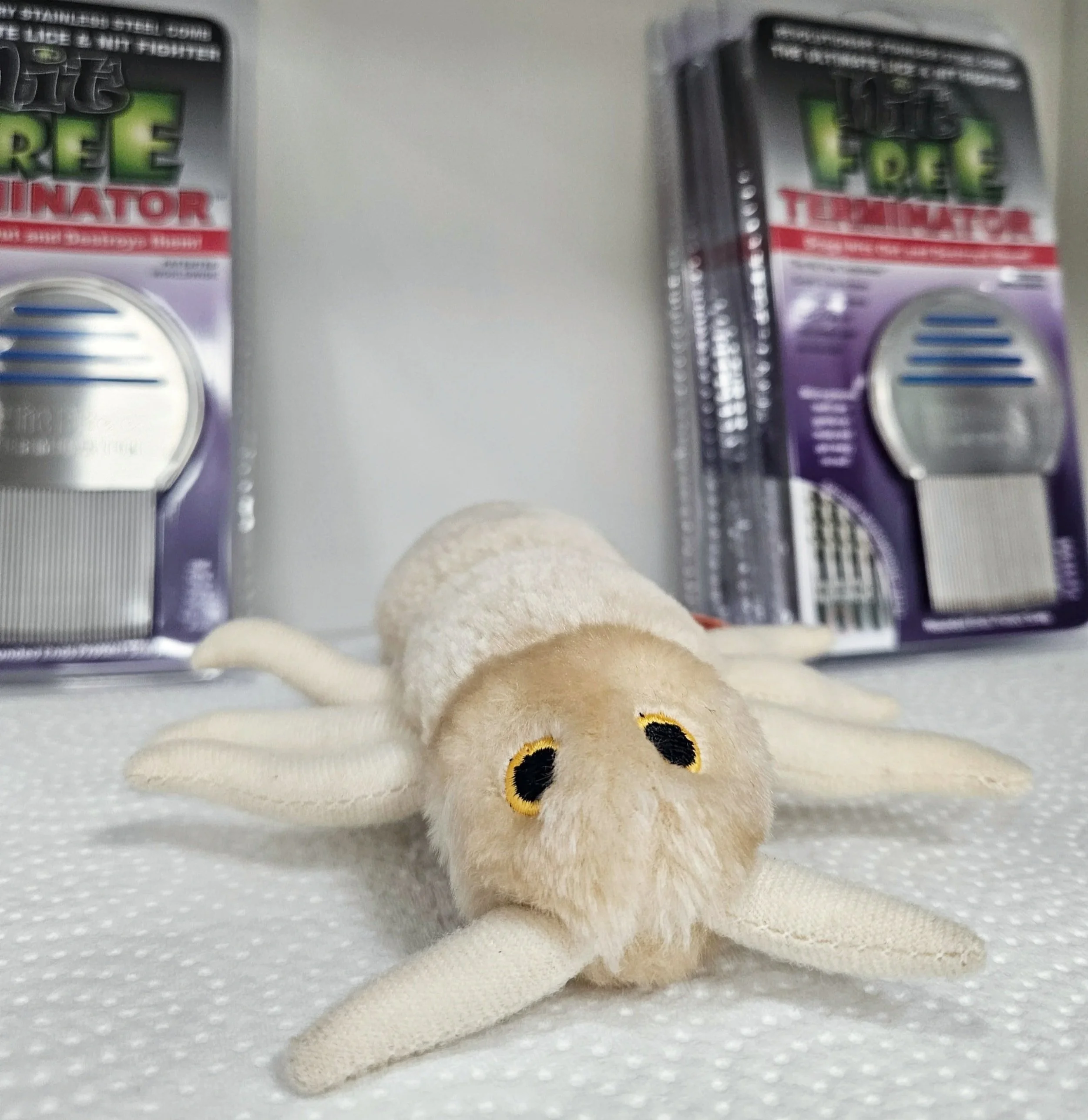 <img source='pic.gif' alt='A plush toy resembling a lice bug with Terminator lice comb. The boxes are black, purple, and white with a circular vent, and the toy is positioned in the bottom center of the image.'.' />.