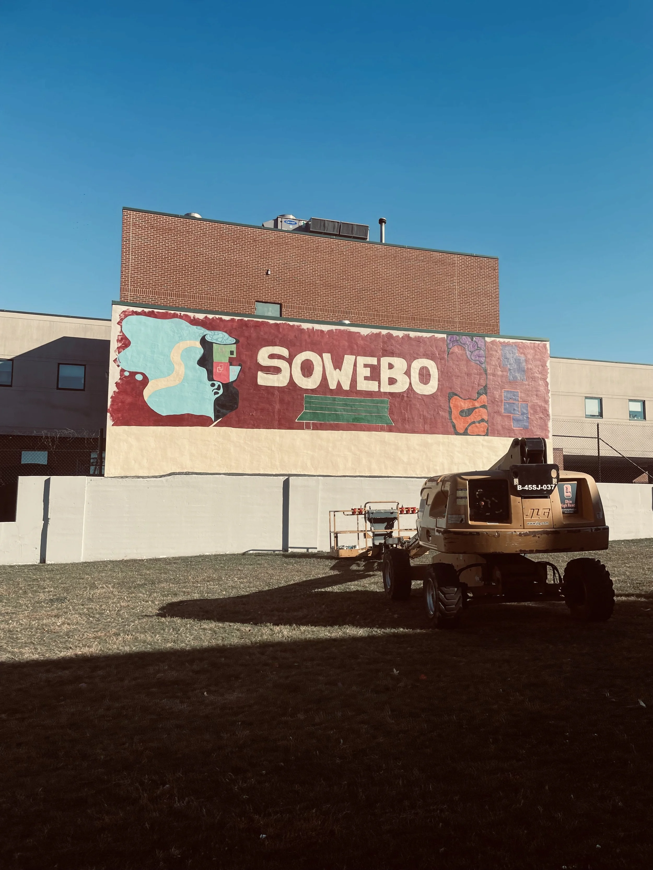 A mural on a building wall that reads 'SOWEBO' with colorful abstract artwork, and a small construction vehicle in the foreground.