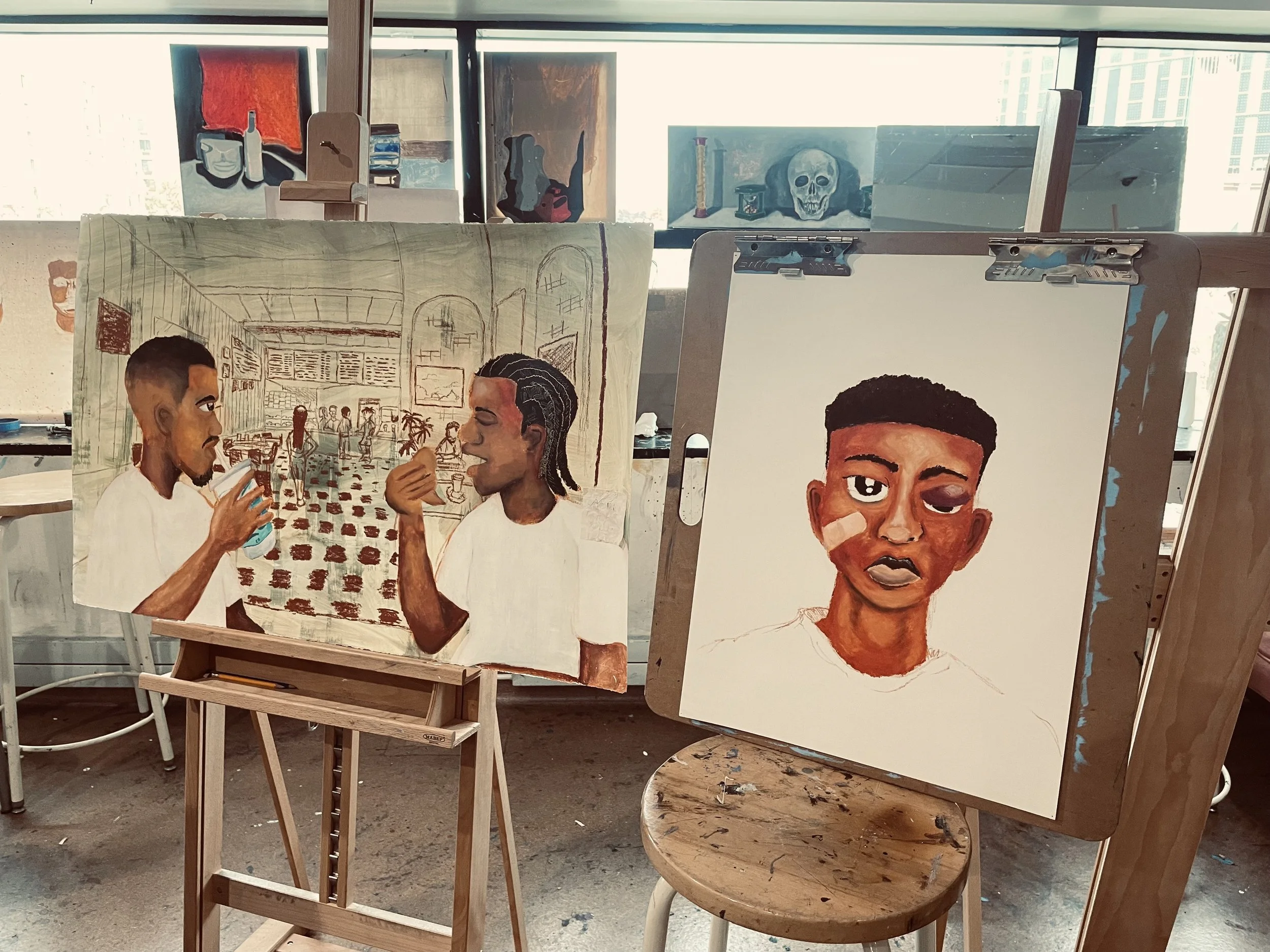 Two paintings on easels, one depicting two young men in a cafe or restaurant, the other a portrait of a young man with a bandage on his cheek, in an art studio with paintings and window with city view in background.
