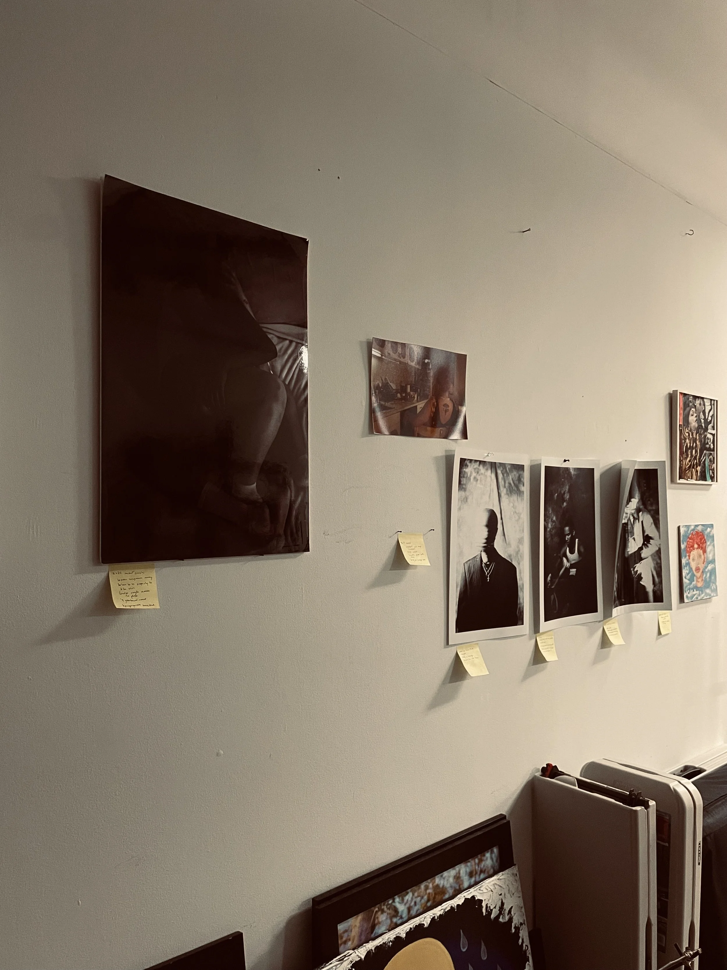 Wall with various photographs and art prints attached with sticky notes underneath, a framed artwork resting against the lower wall, and part of a radiator visible on the right.