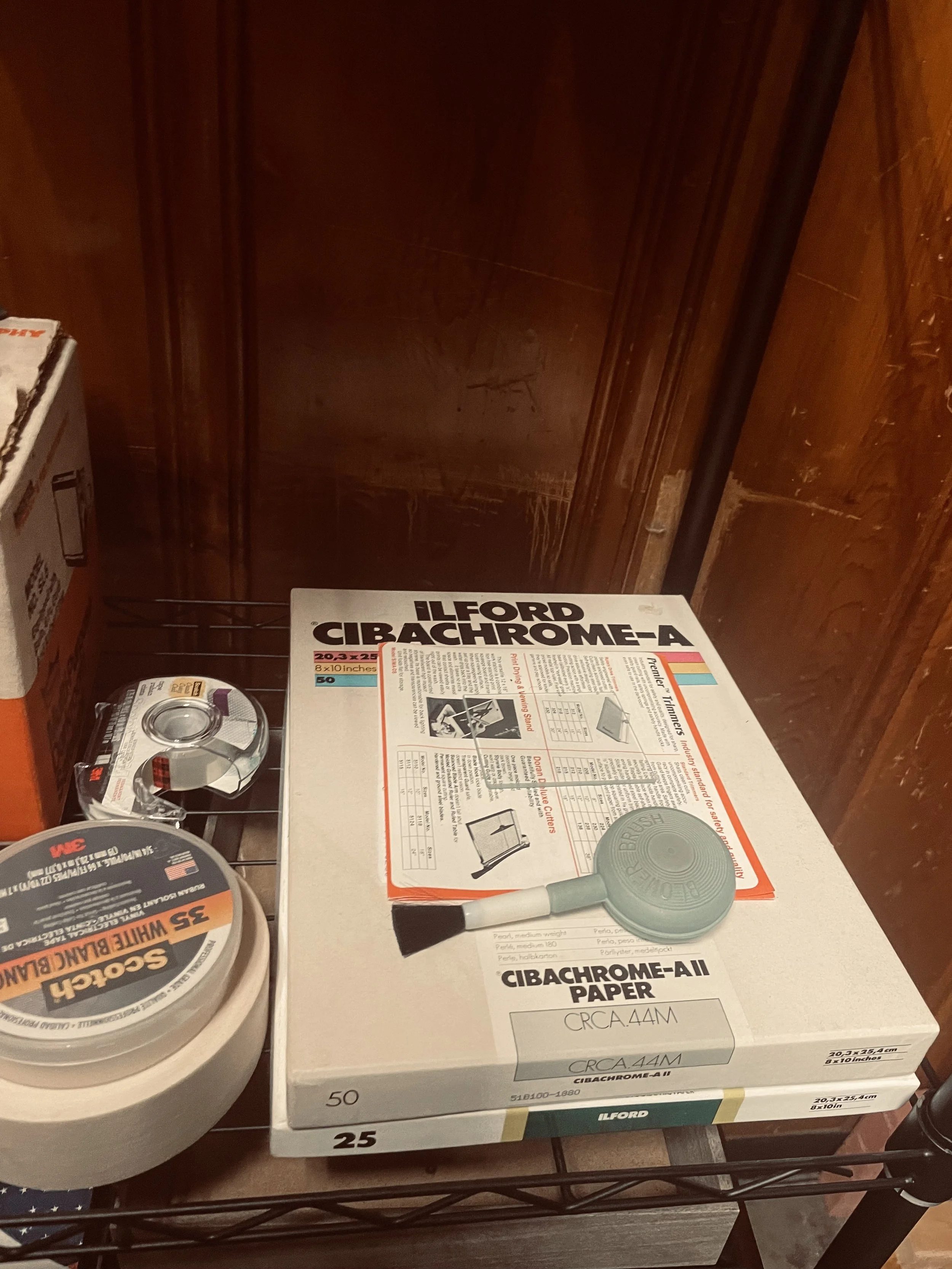 Shelf with tape measure, sanding disc, and ream of Ilford Cibachrome-AII paper for photographic printing.