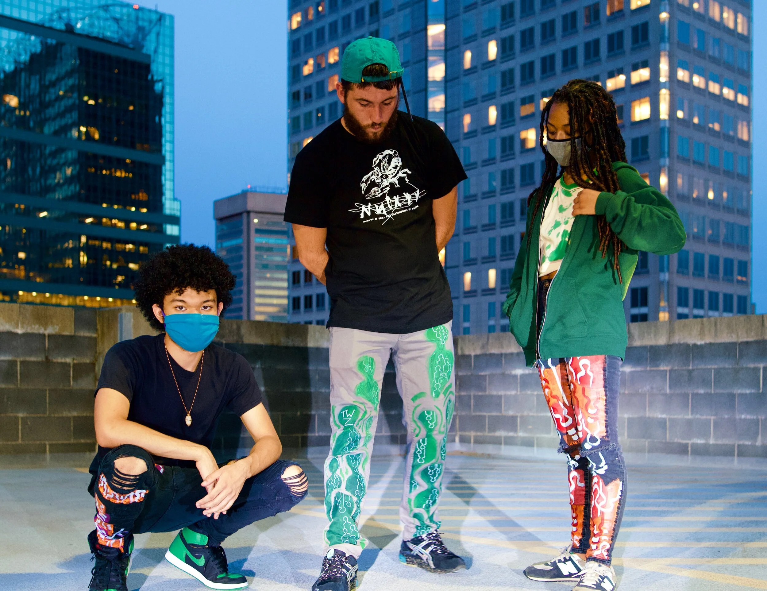 Three young people with masks standing on a rooftop parking lot in an urban area with tall buildings in the background.