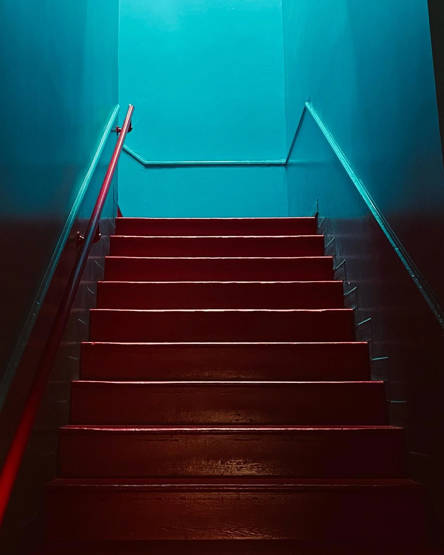Red wooden staircase with metal railings on both sides leading up to a blue wall.