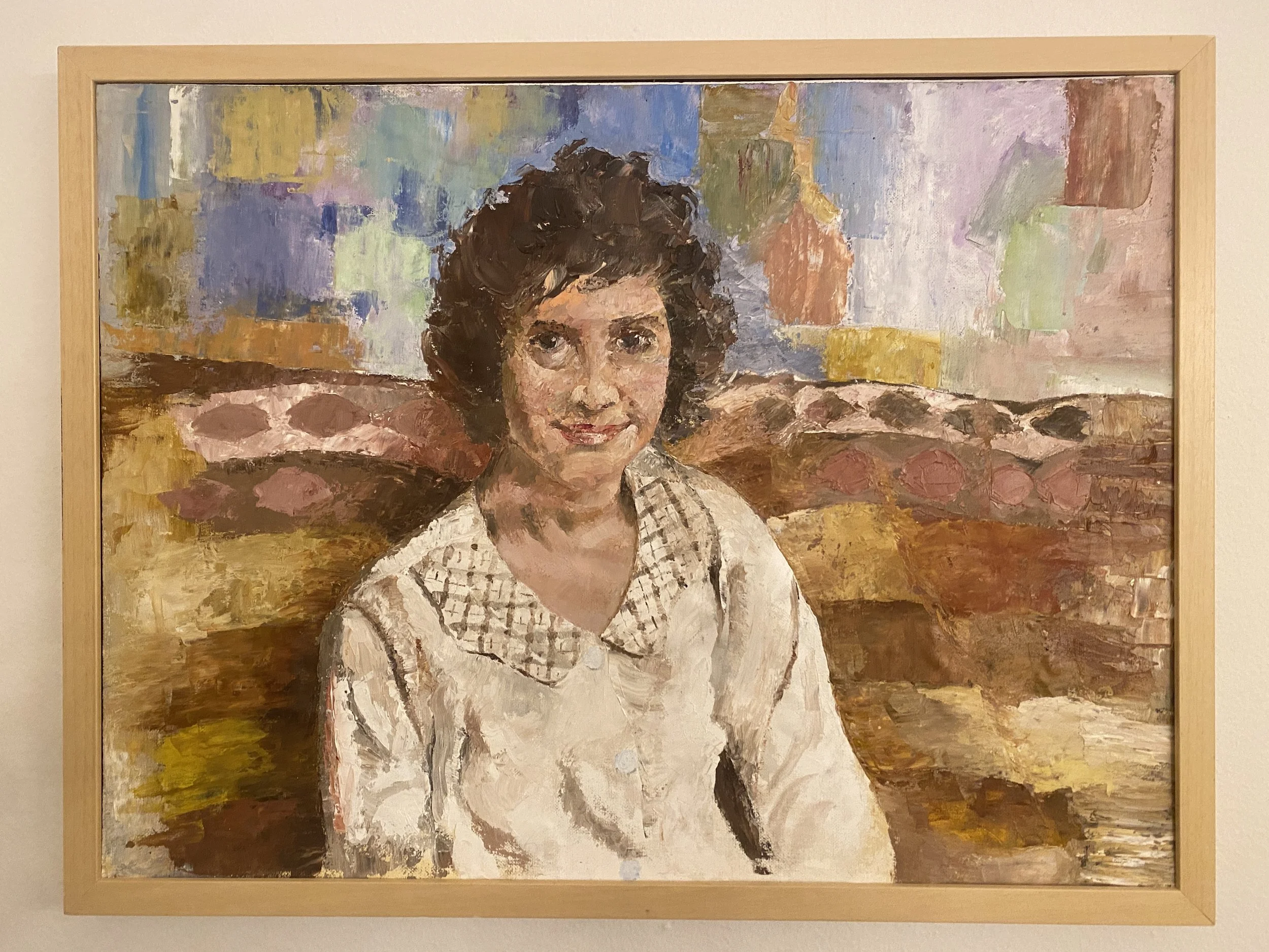 Painting of a woman with dark, curly hair, wearing a white top with a checkered scarf around her neck, in a colorful background.