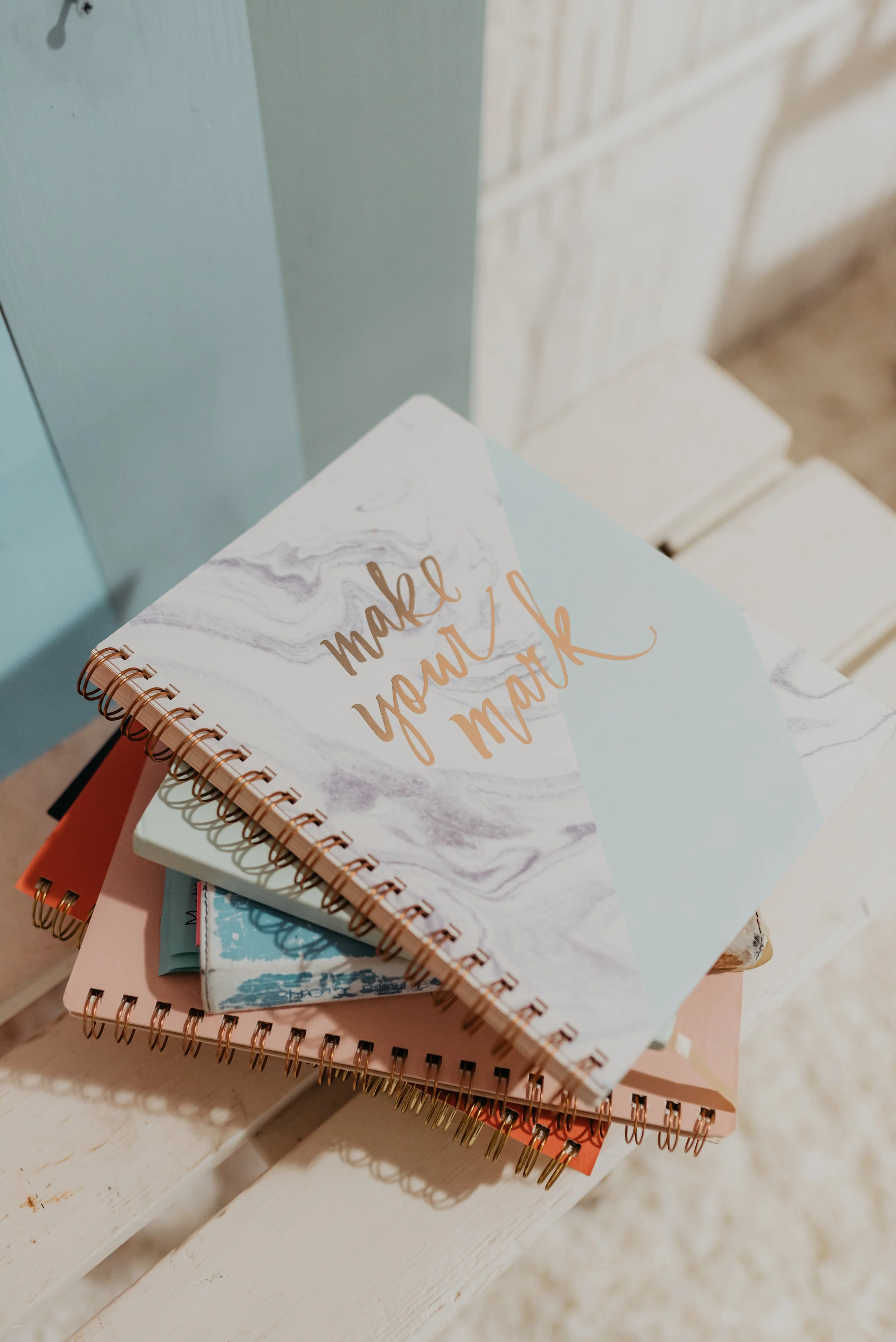 Stack of colorful notebooks with marble and pastel covers, with the top notebook reading 'make your mark' in gold lettering.