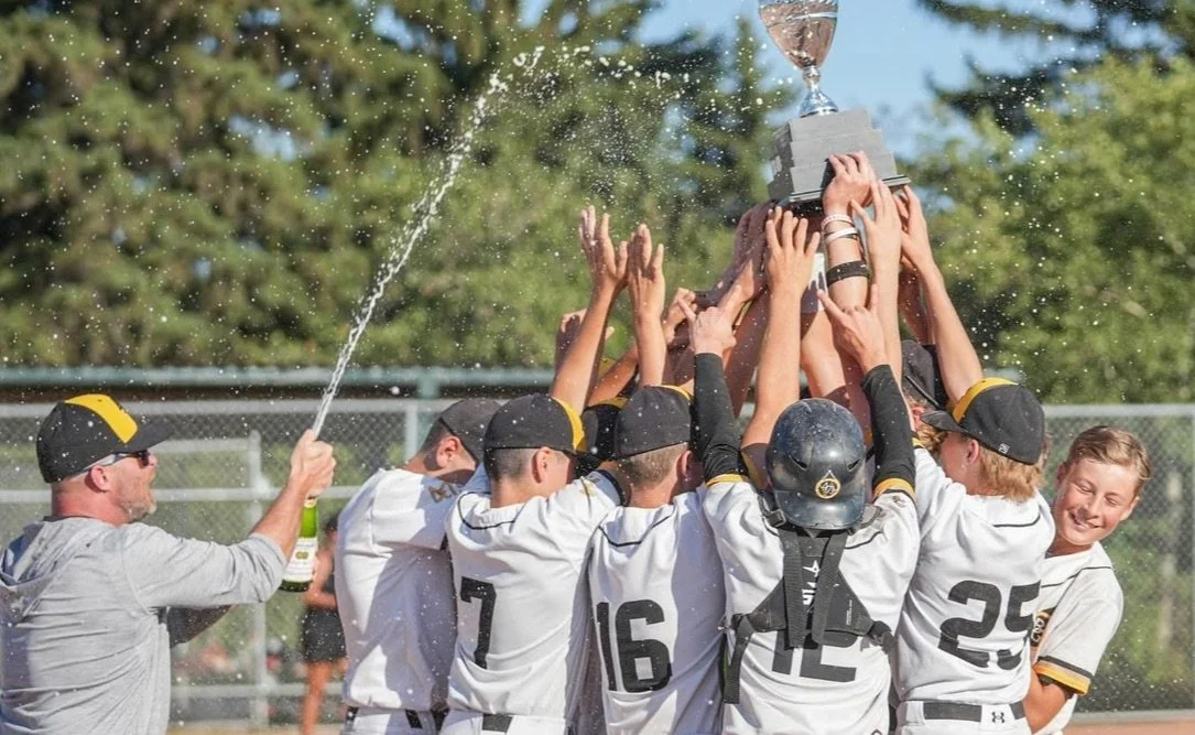 Youth baseball team in uniforms celebrating as they hold up a trophy on the field.