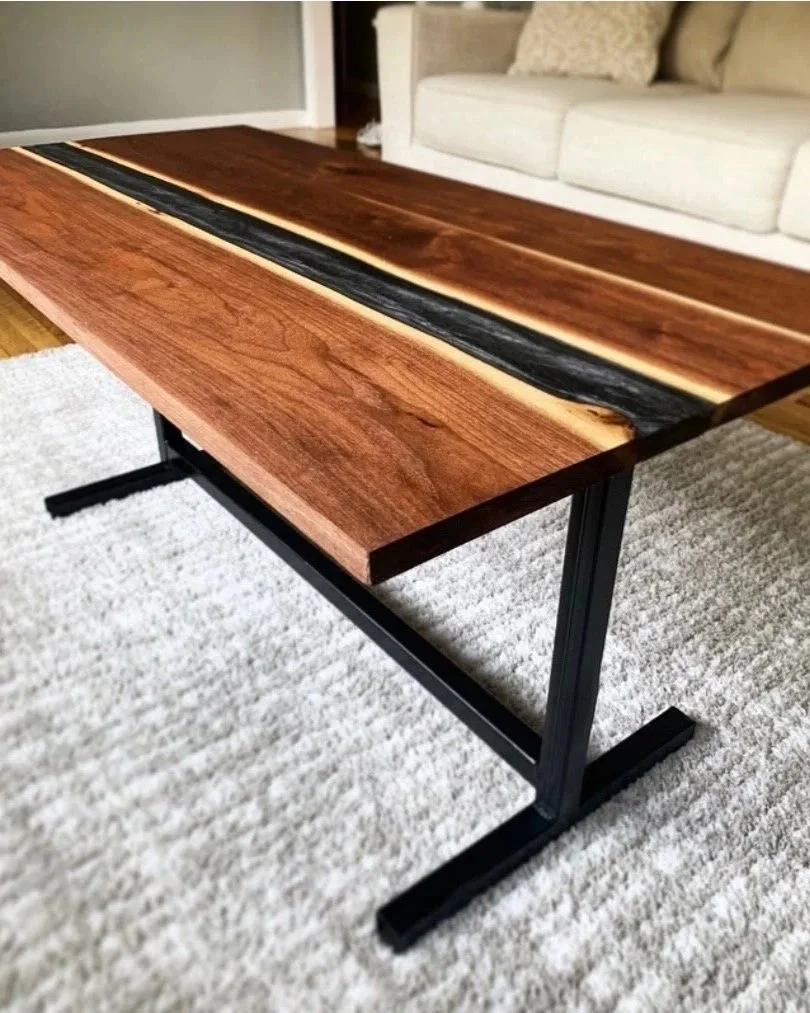 	
Close-up of a walnut river handcrafted wooden coffee table with a natural wood finish and a black resin inlay, situated on a beige carpet in a living room with a white sofa in the background. River table epoxy table. Hand made