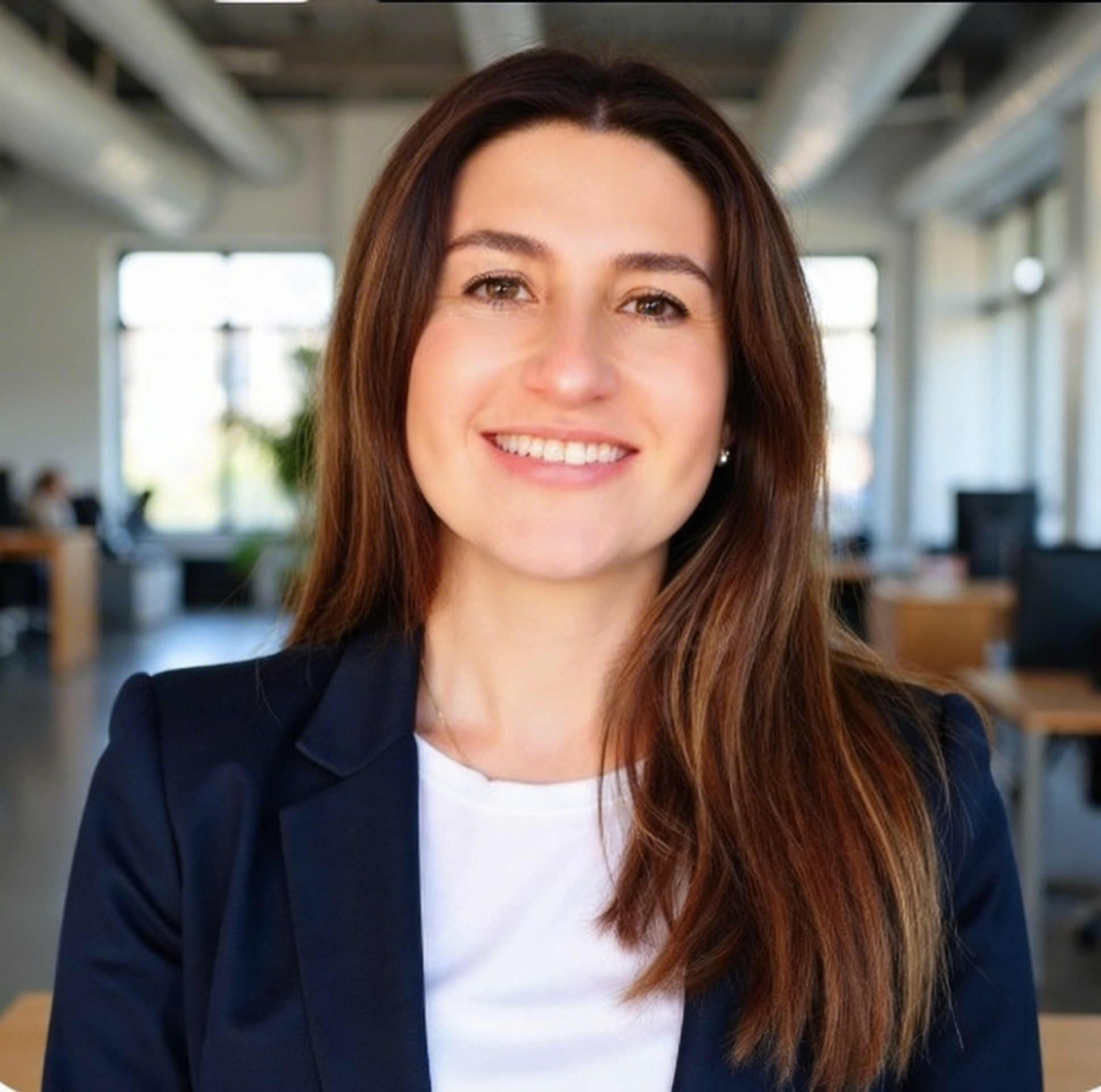 Mujer sonriendo en oficina moderna con fondo de ventanas y computadoras.
