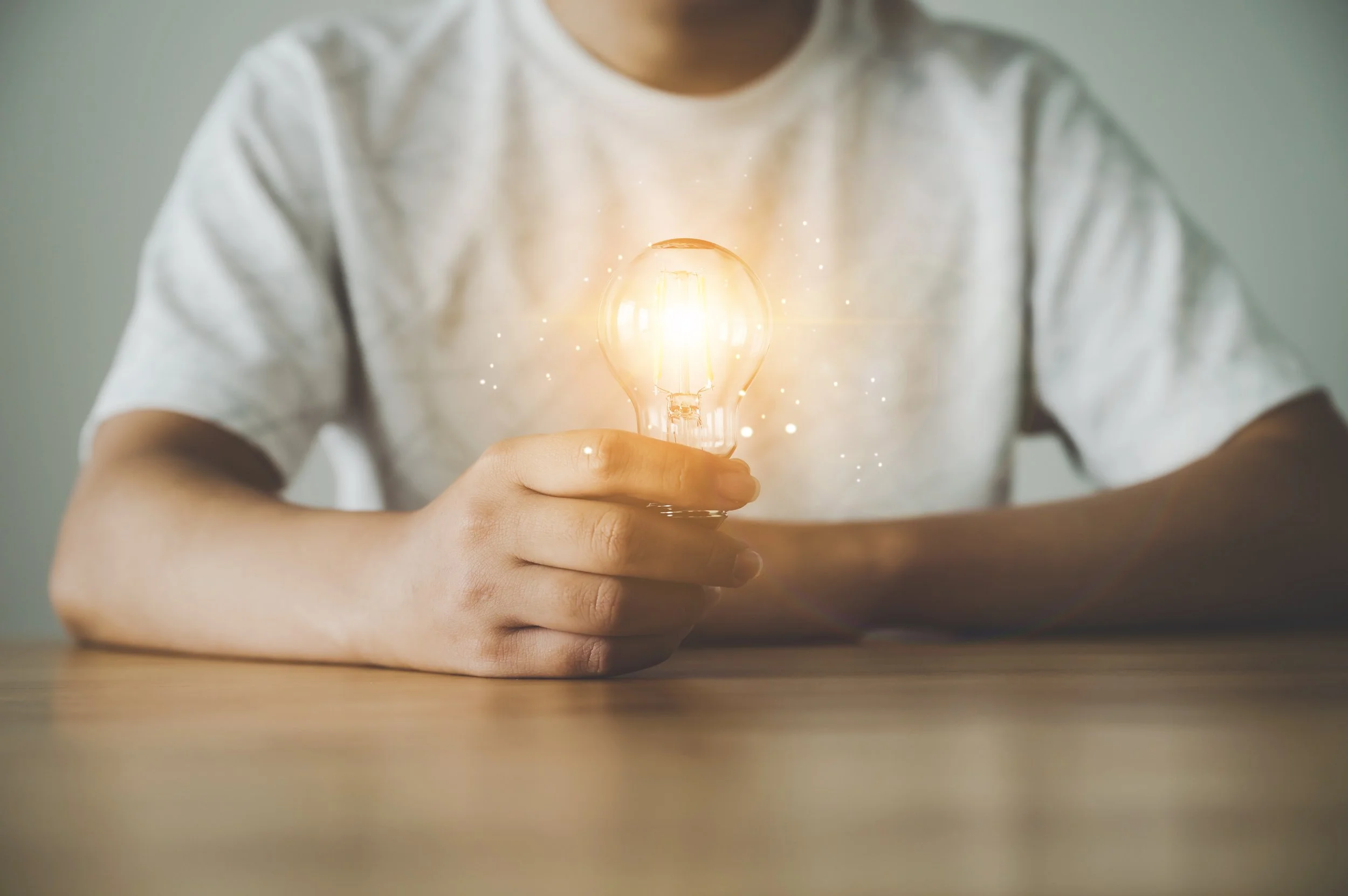 Persona sosteniendo una bombilla con luz brillante y efectos de chispa
