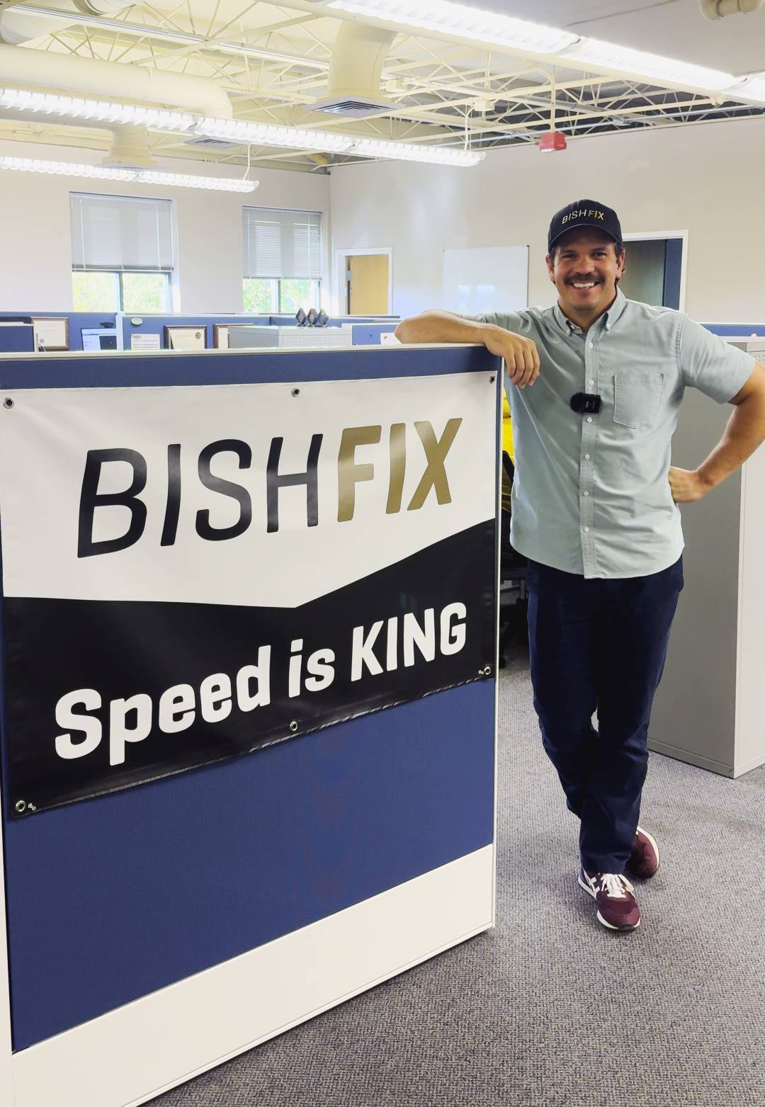 A historical photo of the Director of RVFix standing by a banner with the old BishFix logo