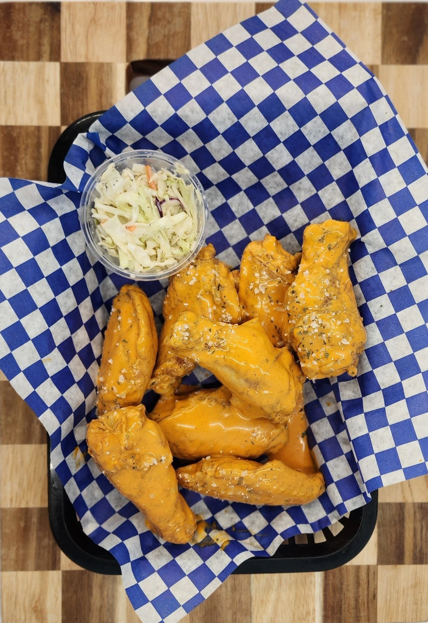 Basket of buffalo chicken wings with orange sauce and a side of coleslaw in a small cup.