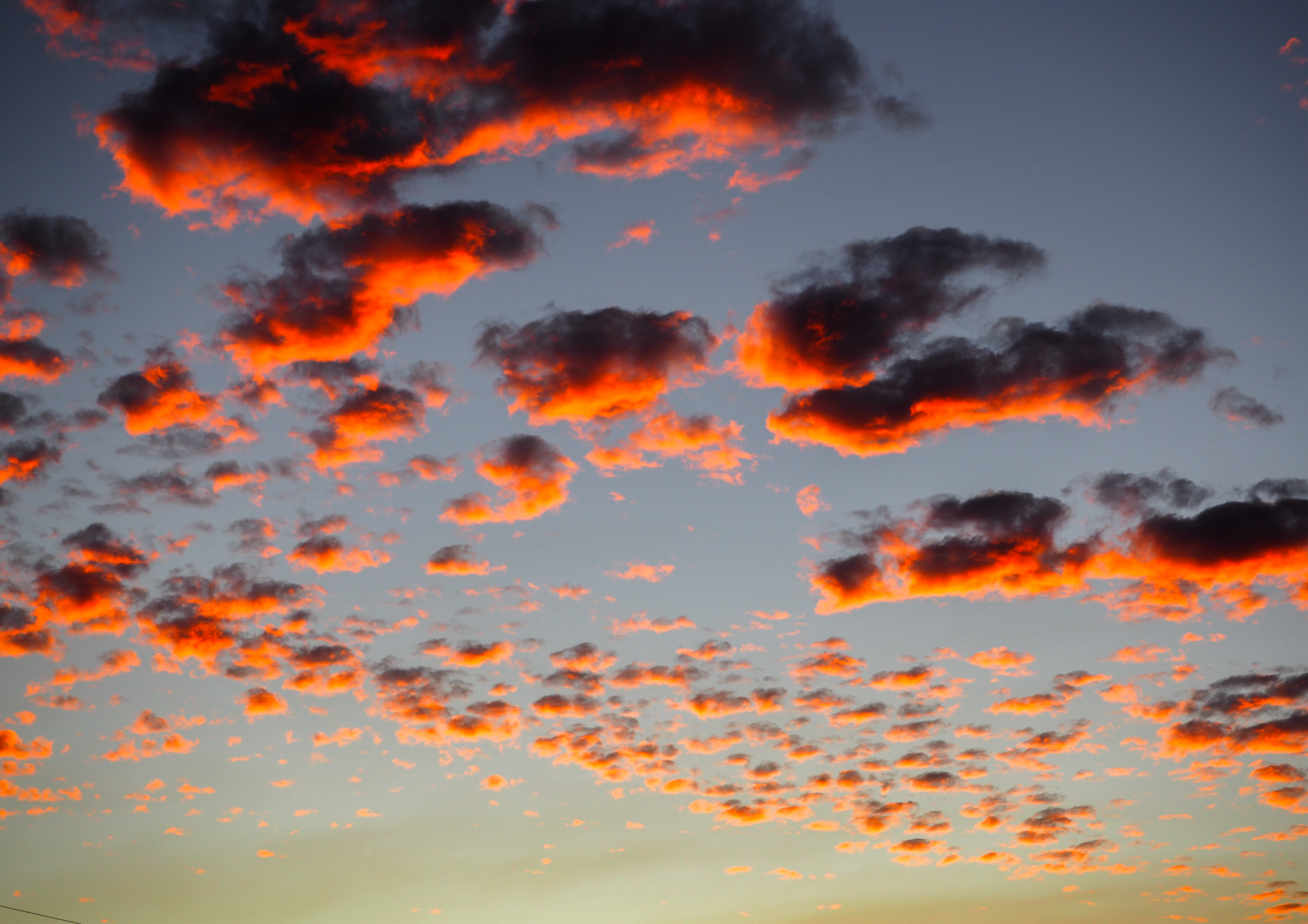 A sky at sunset with dark clouds that are lit with bright orange and red hues.