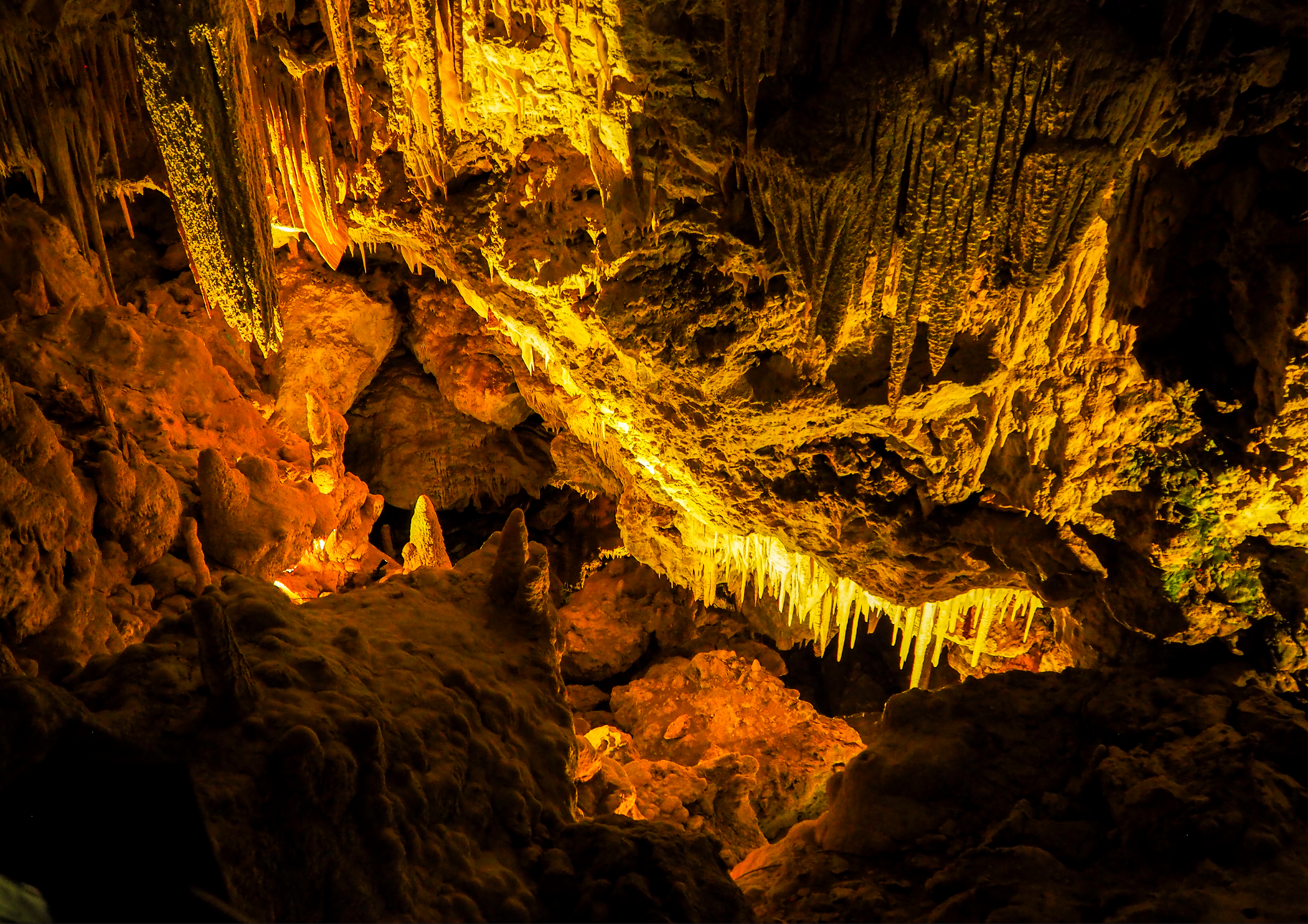 Inside a cave with stalactites and stalagmites illuminated by yellow-orange lighting.